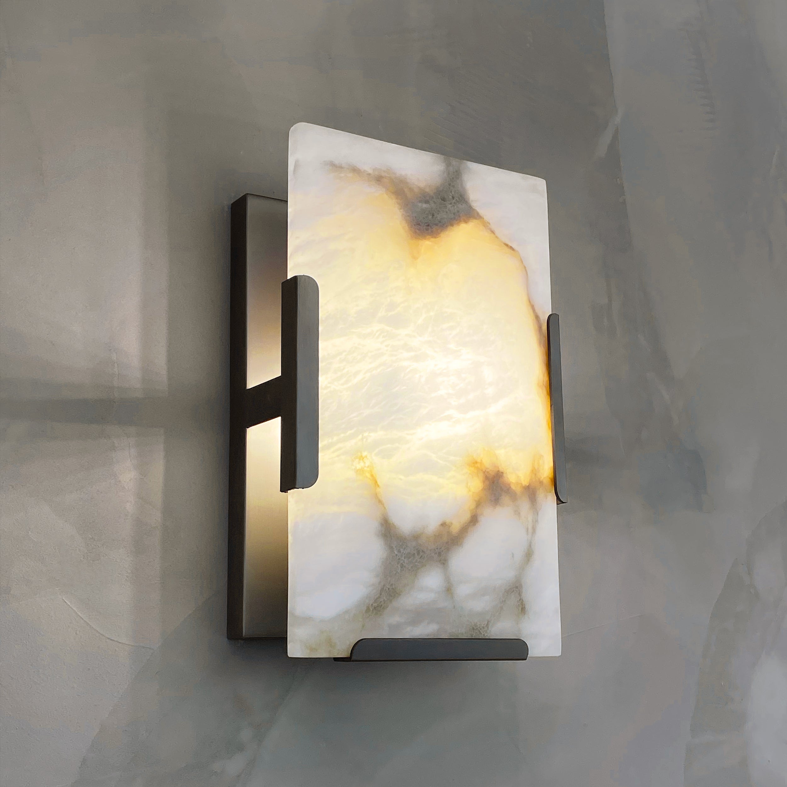 Angel Marble Wall Light featuring sculptural veined marble and industrial black framing, mounted against a grey wall.
