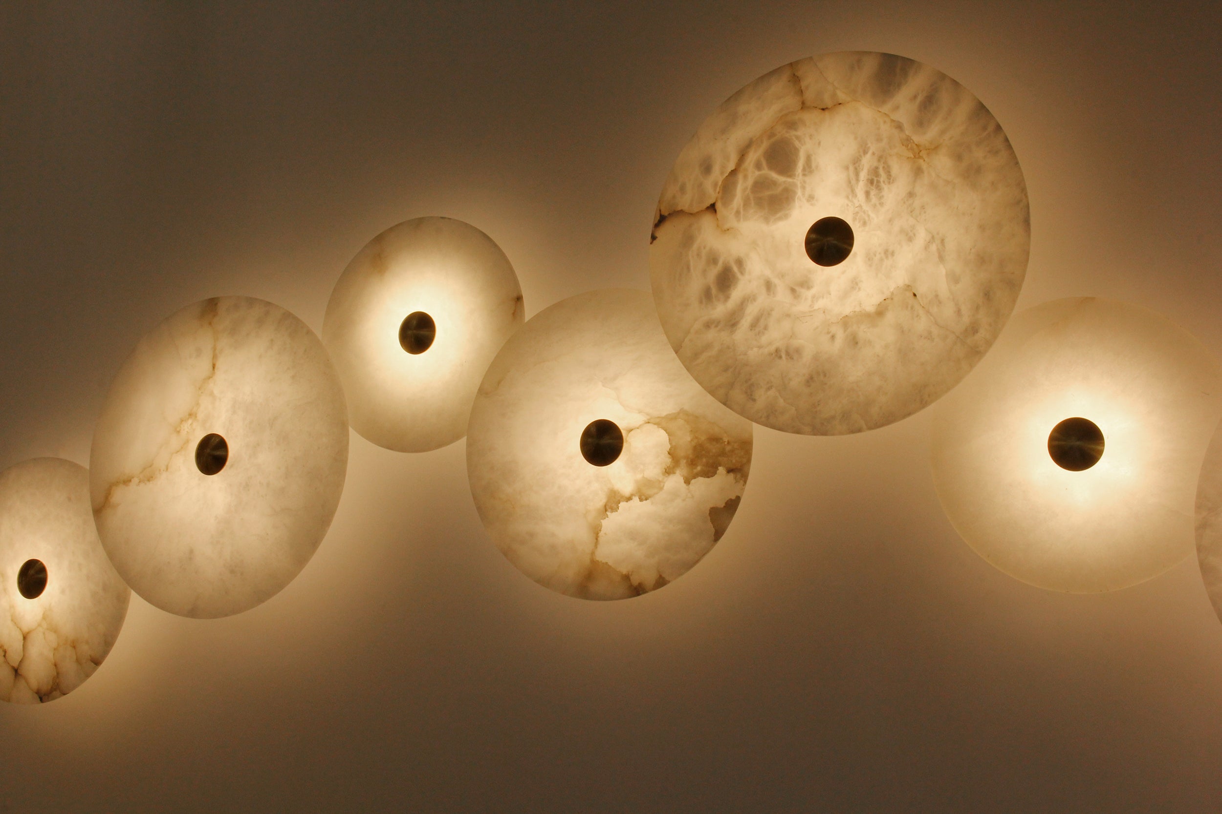 Softly glowing Aria wall light emphasizing natural marble veining and brass centre.