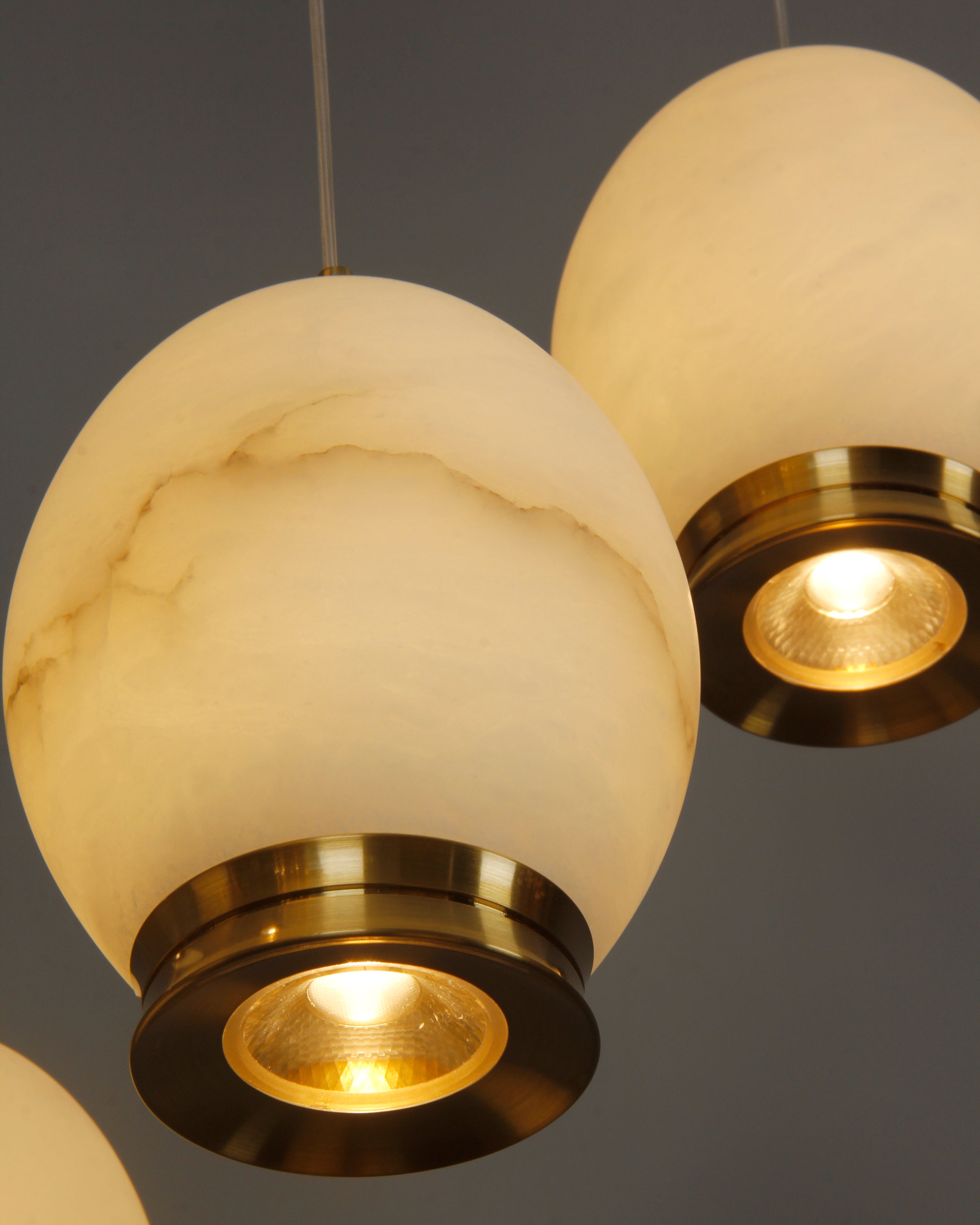 Close-up of Caledonia chandelier marble shade with natural veining and polished brass cap.