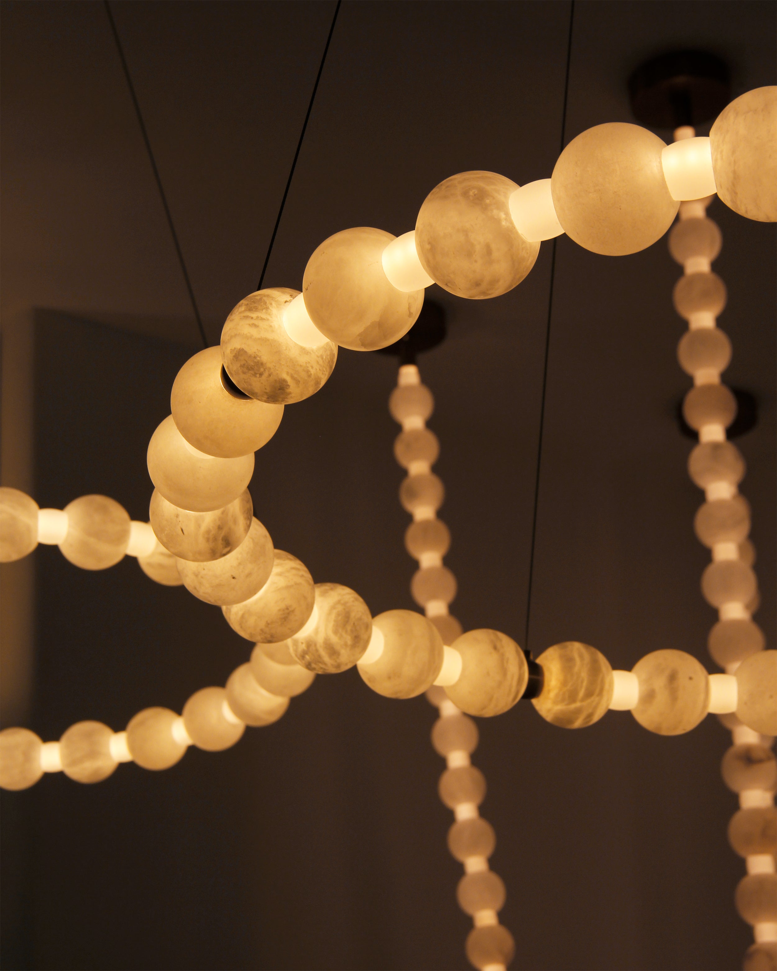 Close-up of Orbella circular chandelier showing smooth marble spheres and soft illumination.