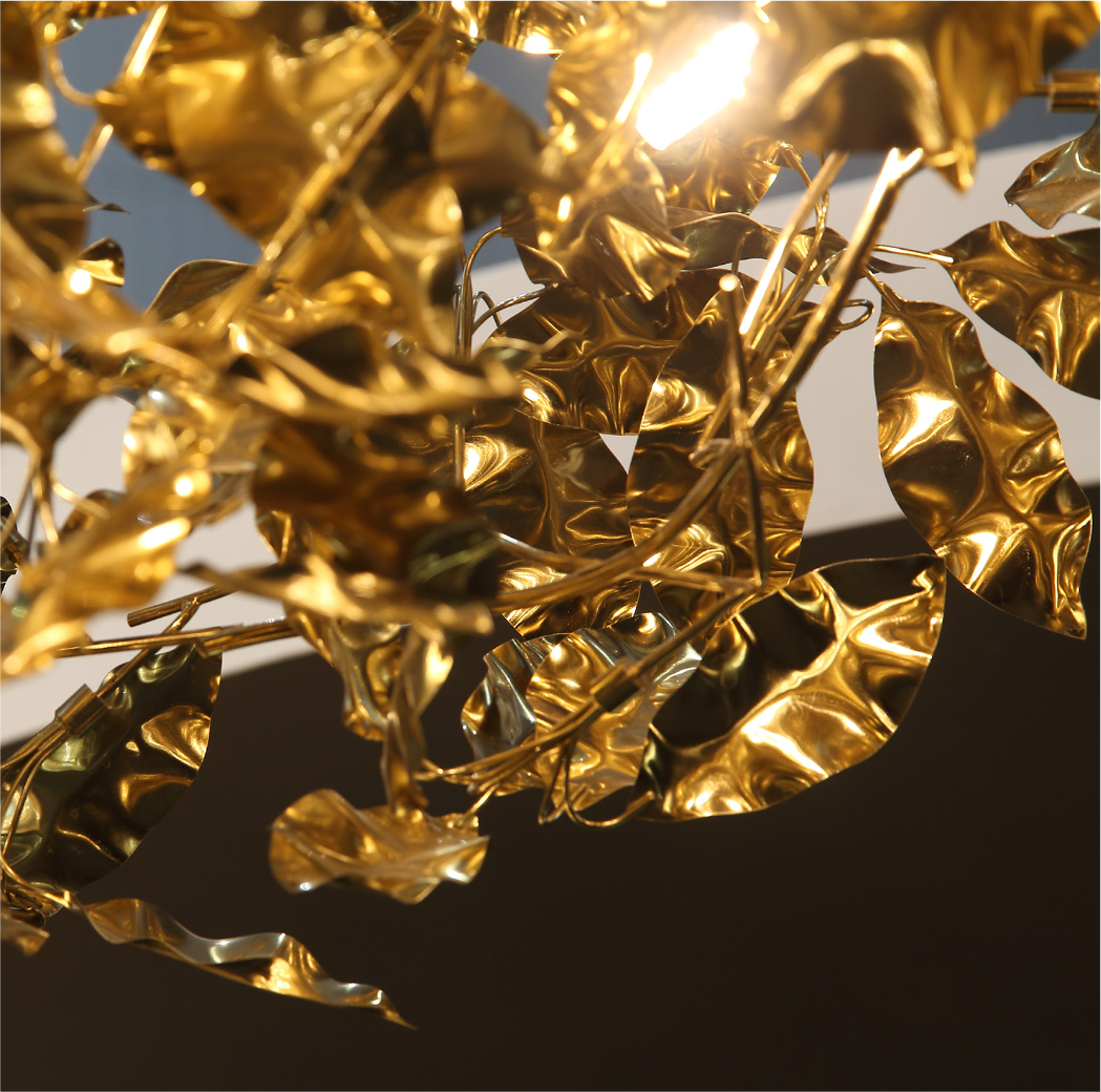A dramatic low-angle view of the VORELLI Aureus Chandelier suspended in a classical spiral stairwell, creating an organic canopy of golden light.