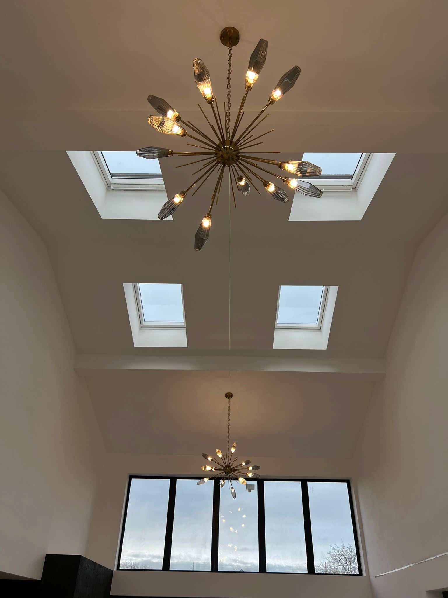 Luxury Abdera pendant light installed in a double-height staircase, featuring sculptural glass rods and warm ambient lighting in a modern UK interior