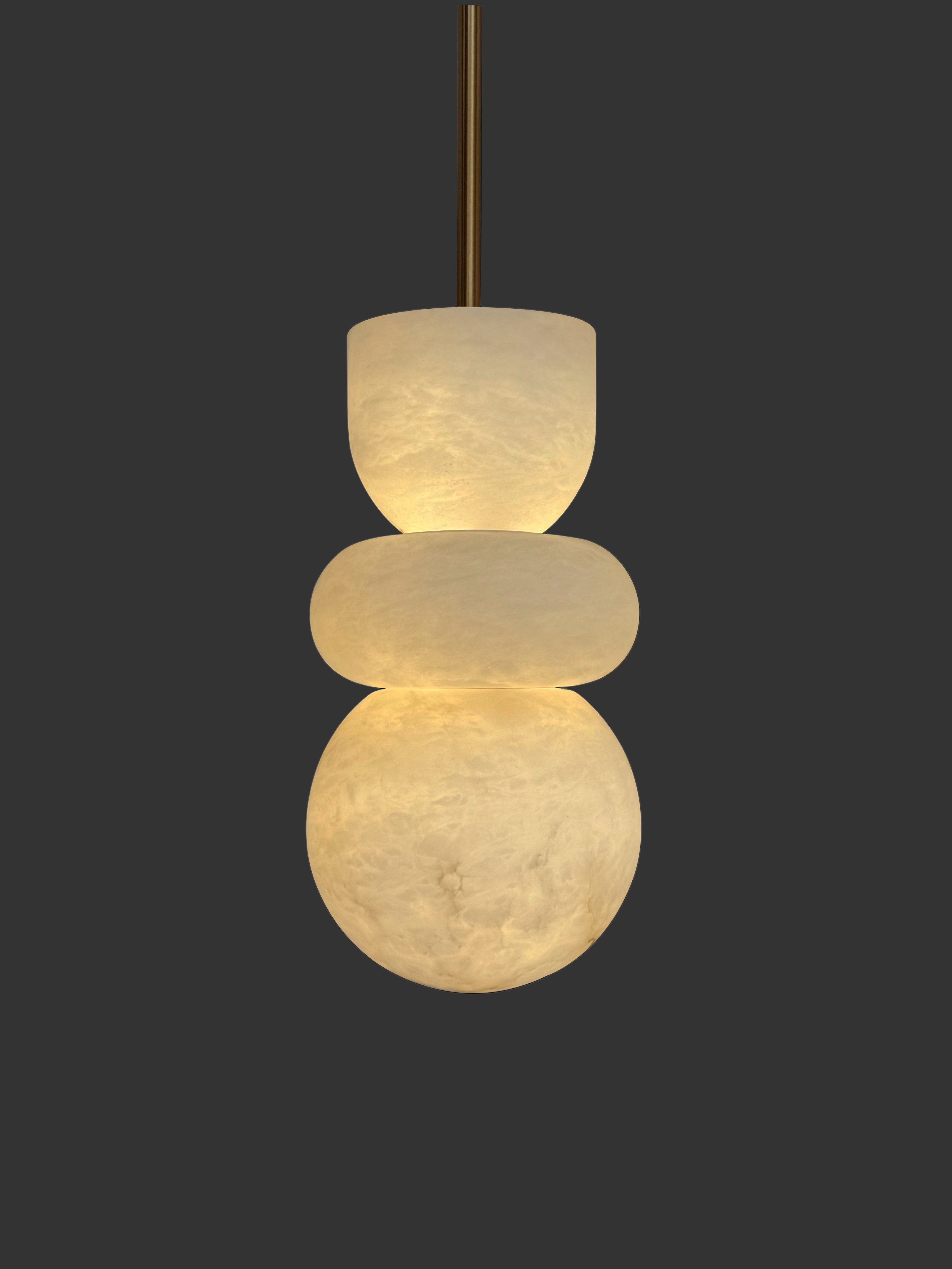 Sculptural pendant light with three stacked glowing marble spheres suspended from ceiling.
