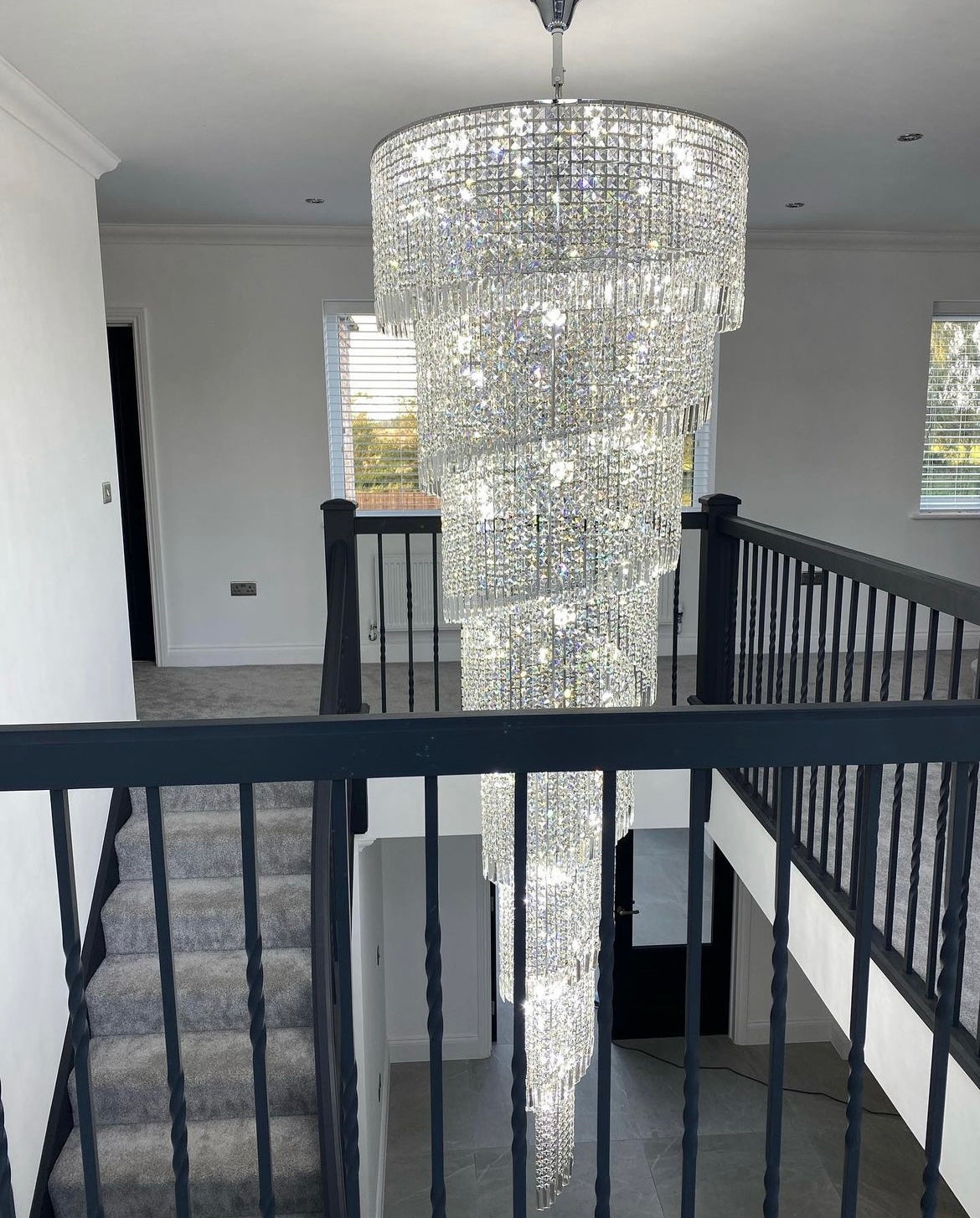 Mid-staircase view of the Basilgio chandelier showcasing layered crystal tiers.