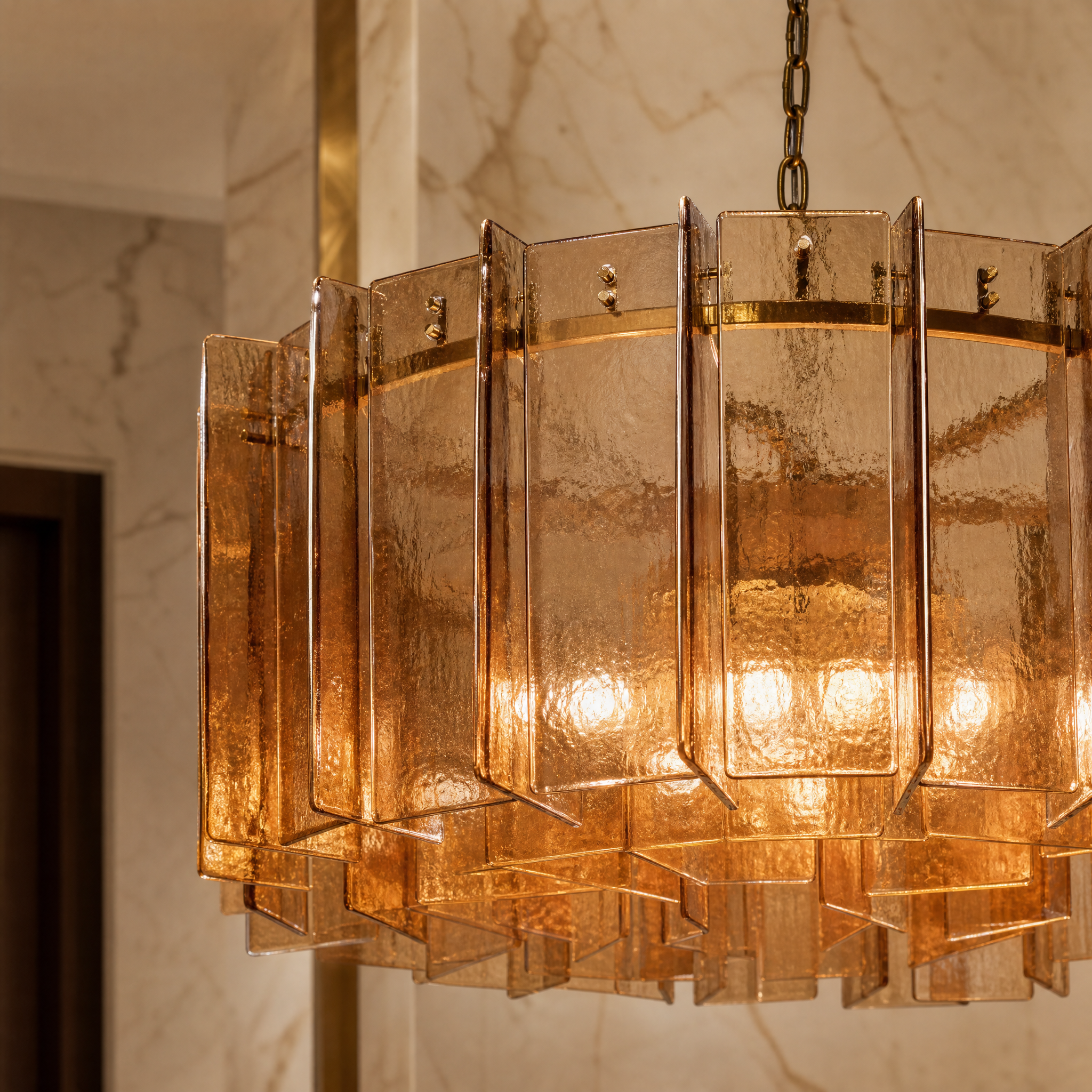 Close-up detail of the Berlinio chandelier showing individually bolted amber glass polyhedrons attached to a polished brass frame.