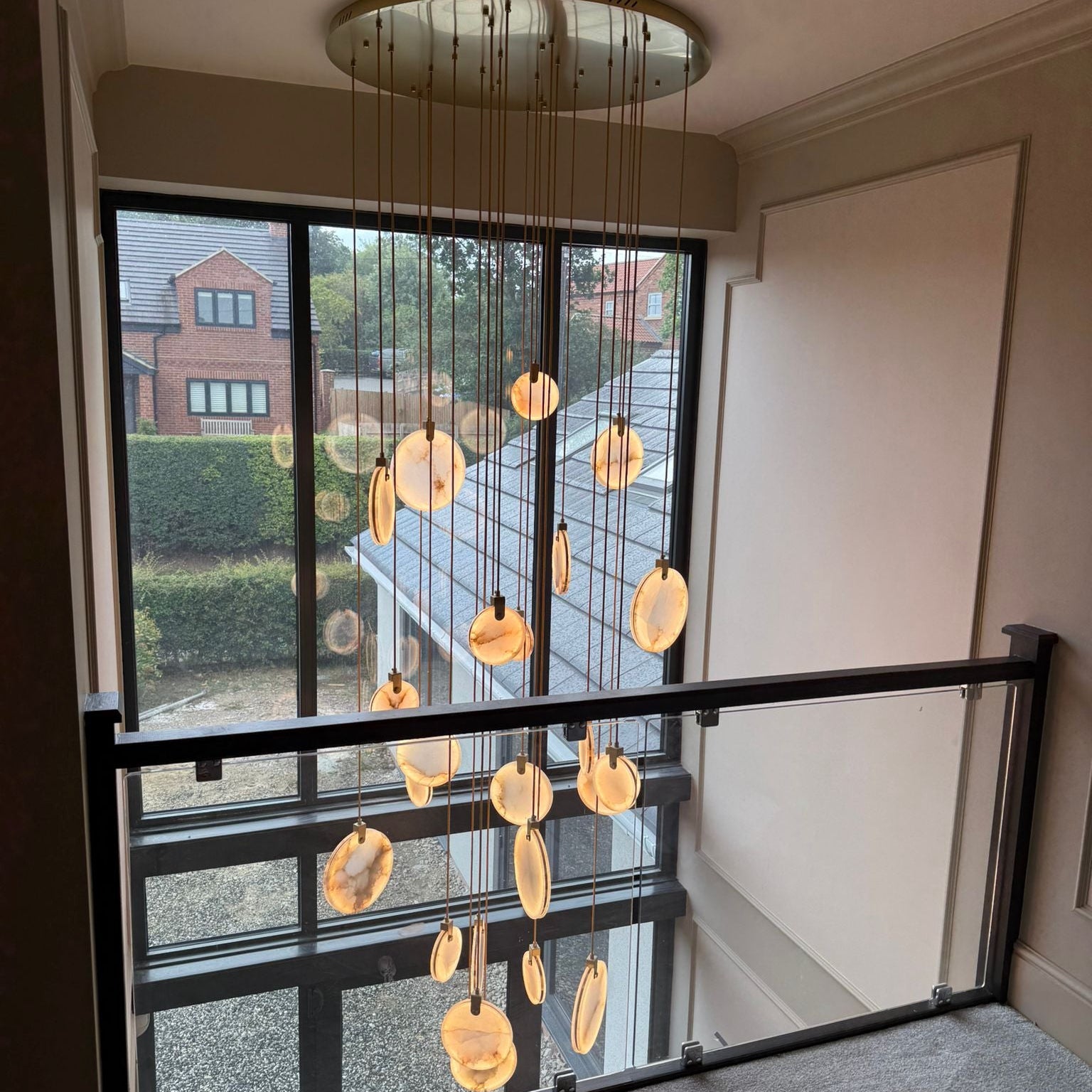 Calacatta marble staircase chandelier viewed from upper landing in a luxury double height interior.