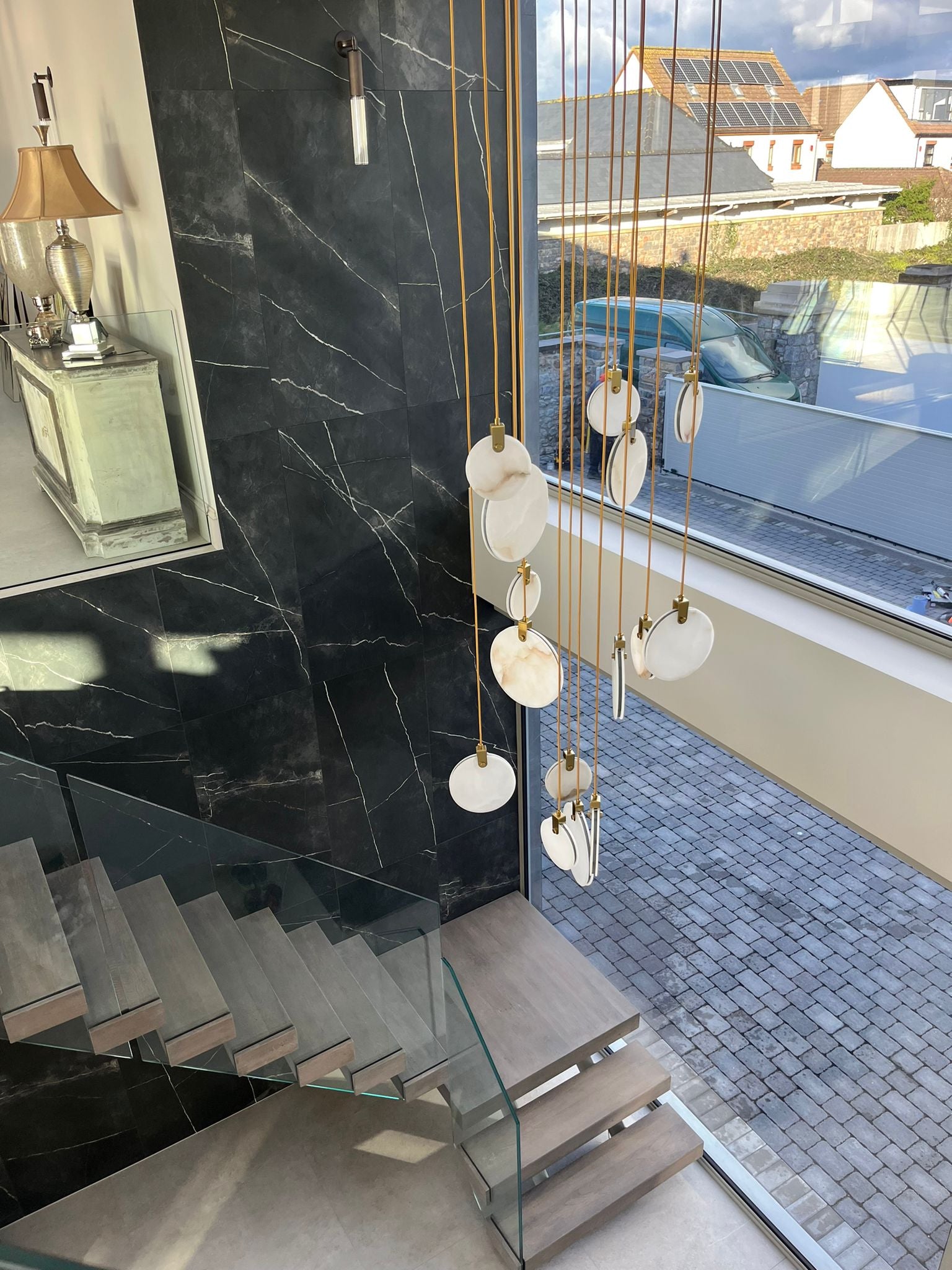 Calacatta marble staircase chandelier installed in a luxury modern home with glass staircase and natural daylight.