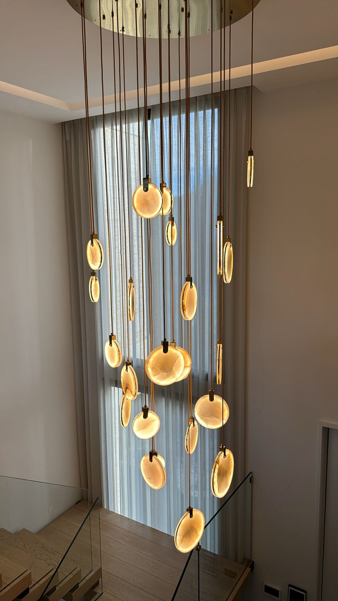 Calacatta marble staircase chandelier with full vertical drop in a double height luxury interior.