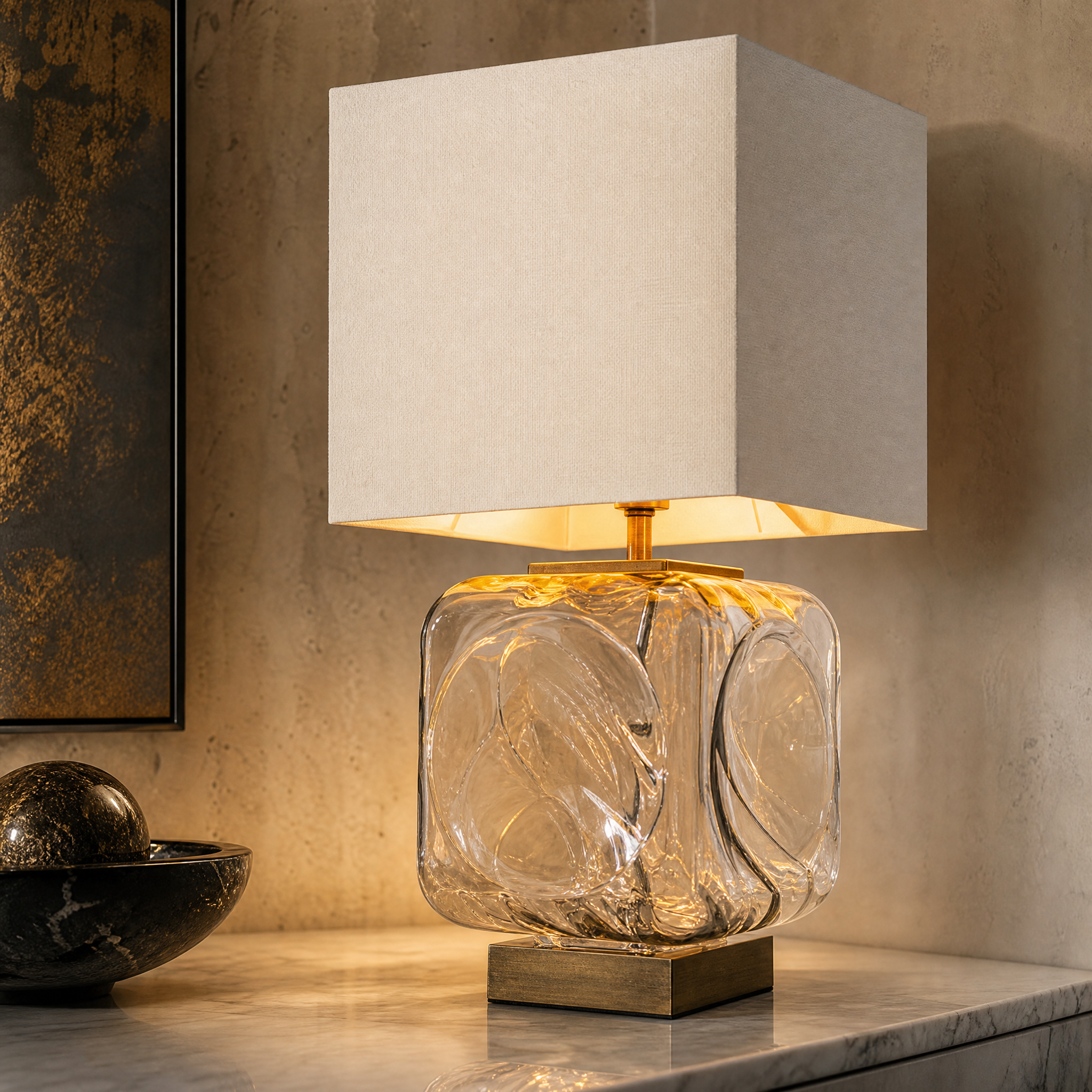 A detailed closeup of the VORELLI Calvoro table lamp, highlighting the textured antique brass detailing, sculpted clear glass base, and structured fabric shade.