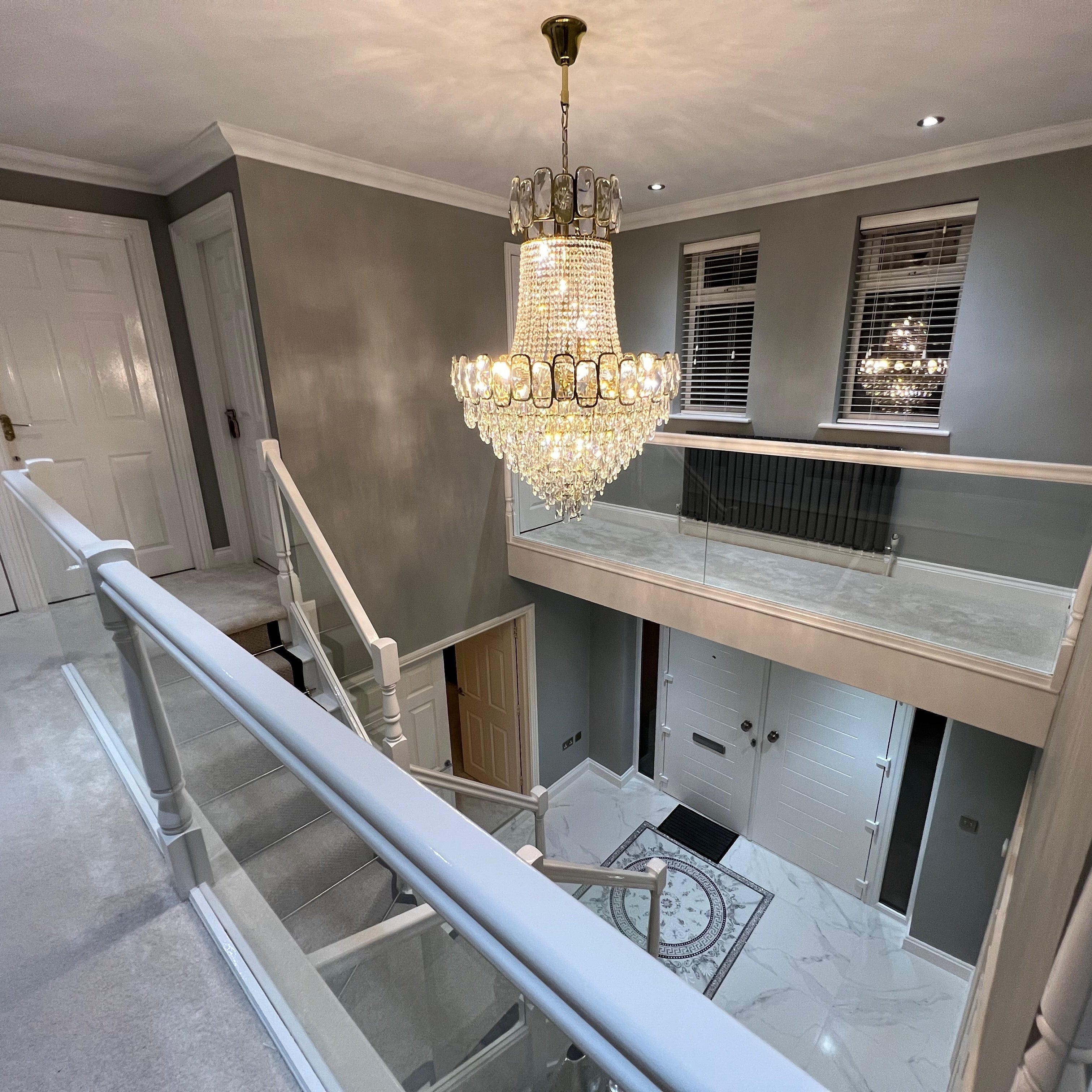 Crystal staircase chandelier illuminating a modern hallway and stairwell, featuring layered faceted crystals and elegant suspended design.