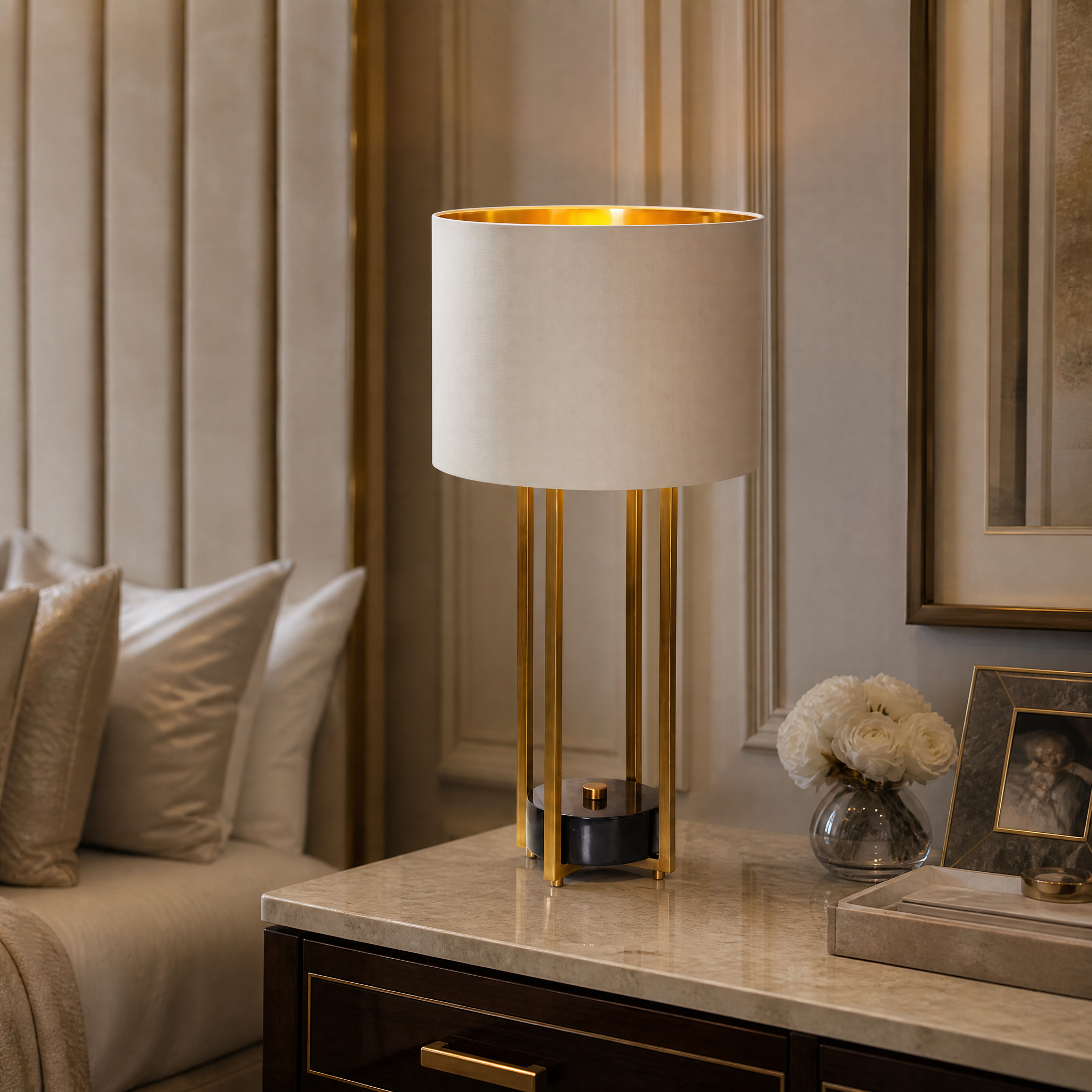 A sophisticated Marzello brass and marble table lamp placed on a wooden side table in a modern residential living room setting.