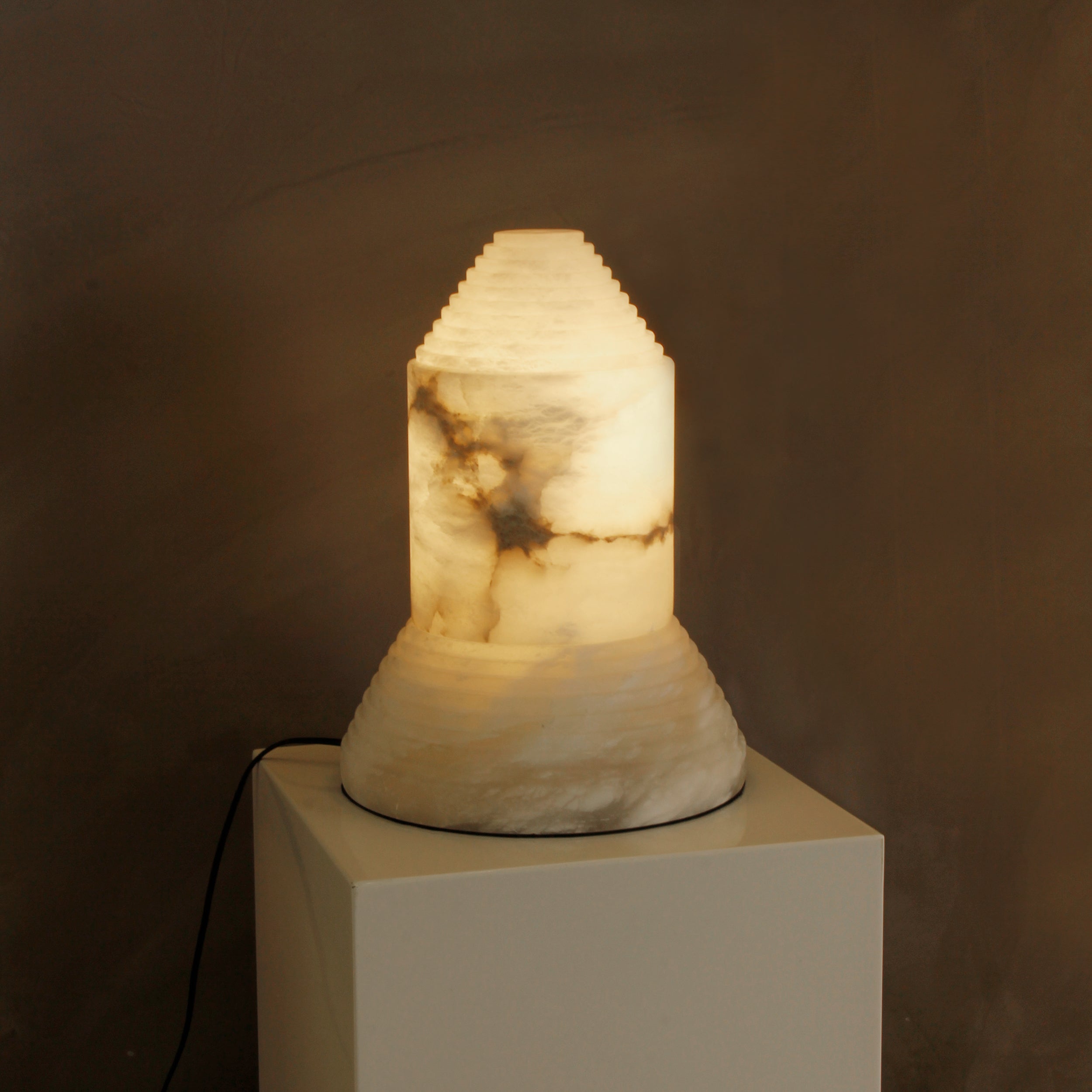 Stratto modern tiered marble table lamp glowing softly to highlight natural stone veining