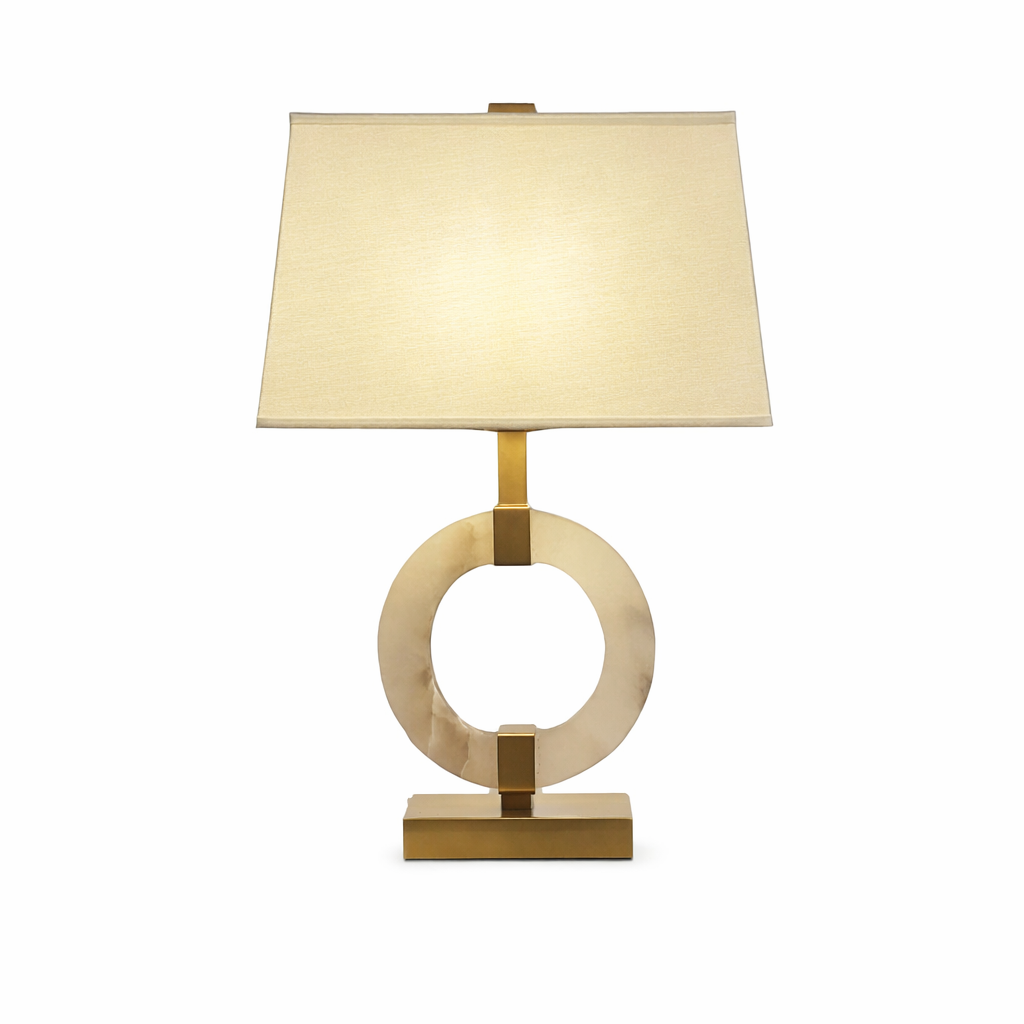 The Anello Marble Table Lamp illuminated against a dark, moody backdrop, emphasizing its geometric circular form and golden radiance.