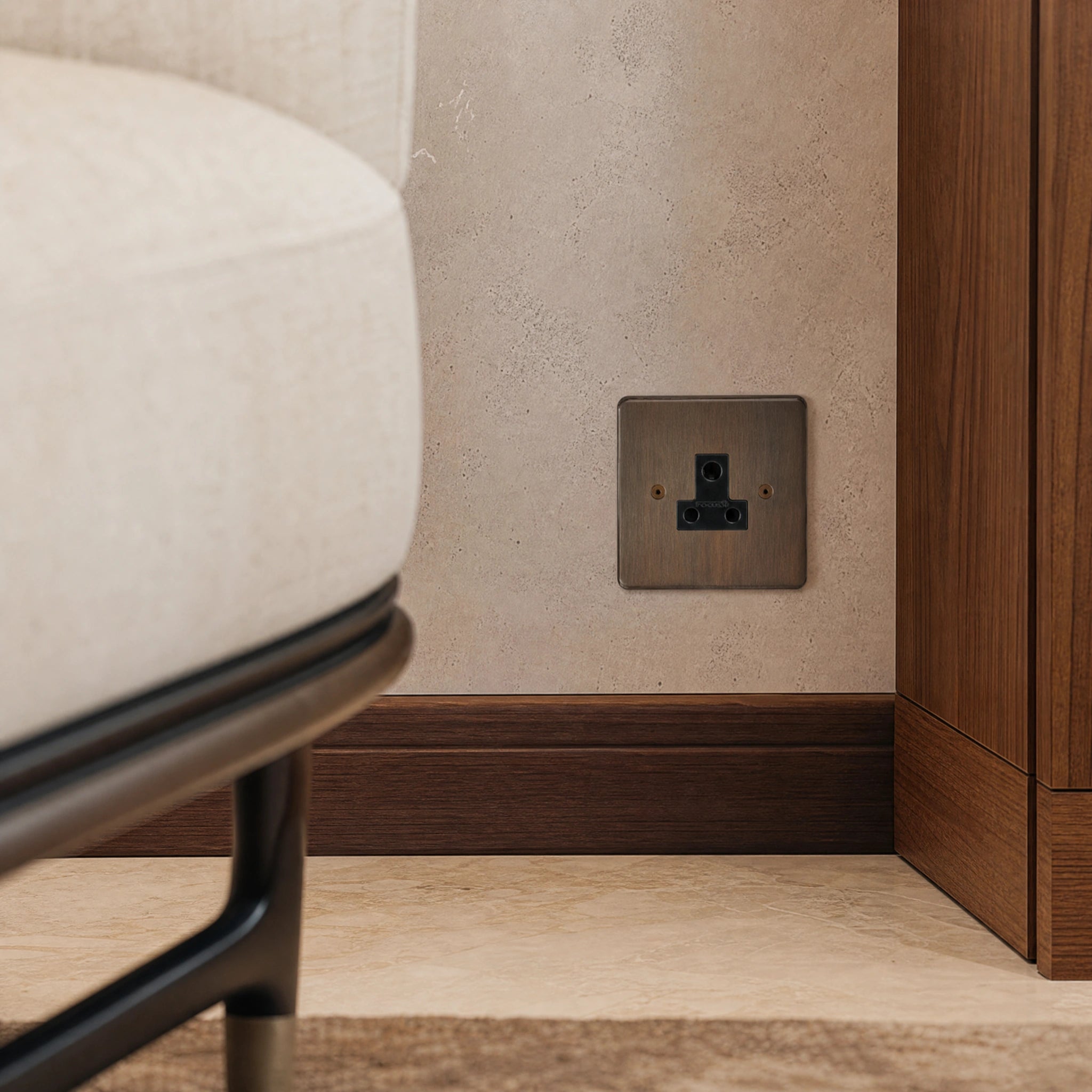 Close-up of a luxury antique brass 5a socket installed within bespoke bedside joinery or low-level wall beside a luxury seating area by VORELLI®.