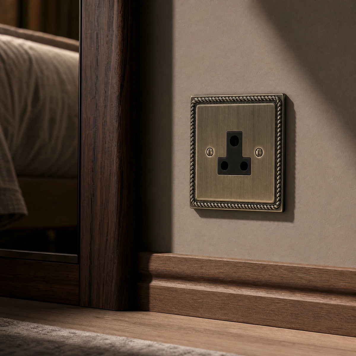 Close-up of a luxury antique brass 5a socket installed within bespoke bedside joinery or low-level wall beside a luxury seating area by VORELLI®.