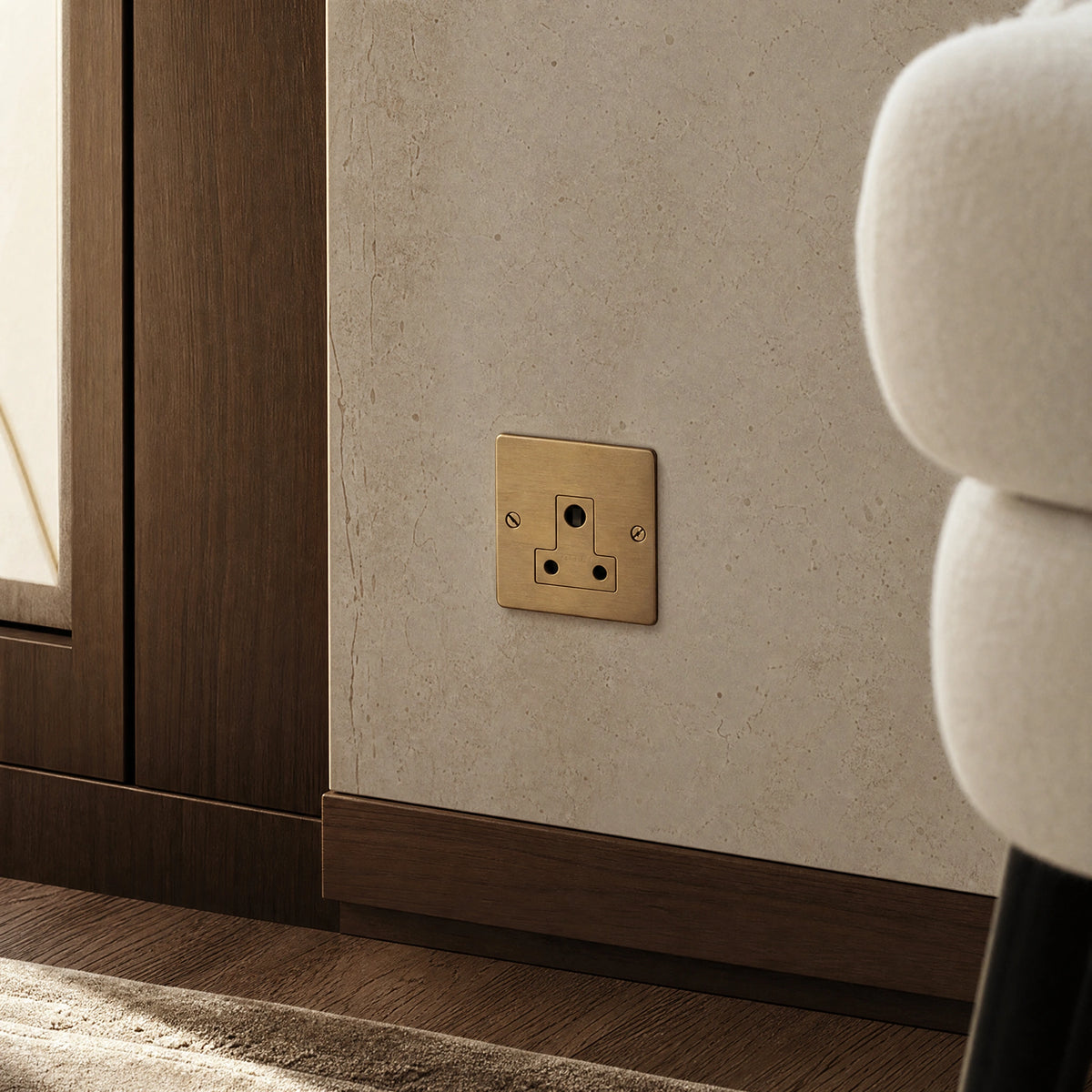 Close-up of a luxury antique brass 5a socket installed within bespoke bedside joinery or low-level wall beside a luxury seating area by VORELLI®.