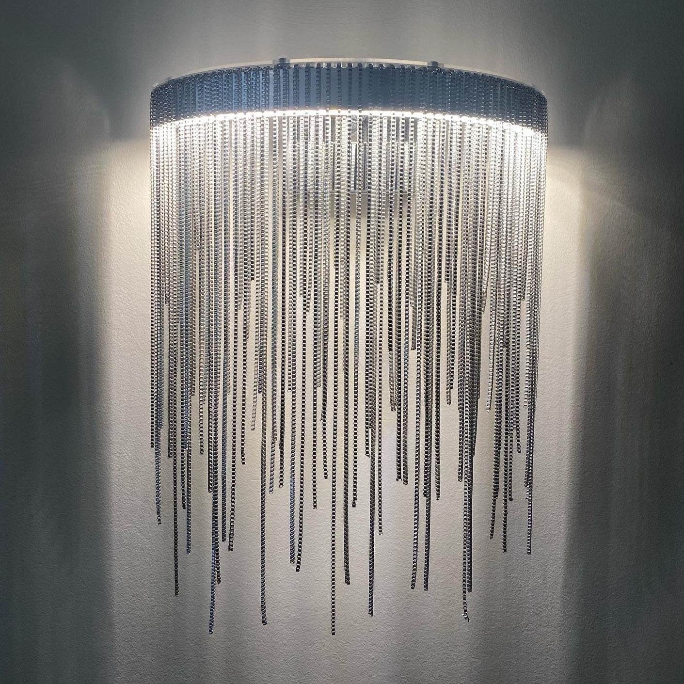 Vertical shot of the Adlington Wall Light emphasizing the upward glow and the shimmering effect of the silver chain tiers.