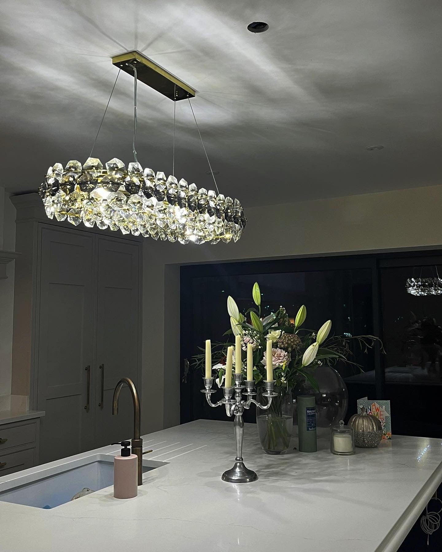 Astoria rectangular chandelier by VORELLI® creating ambient lighting above a luxury kitchen island at night