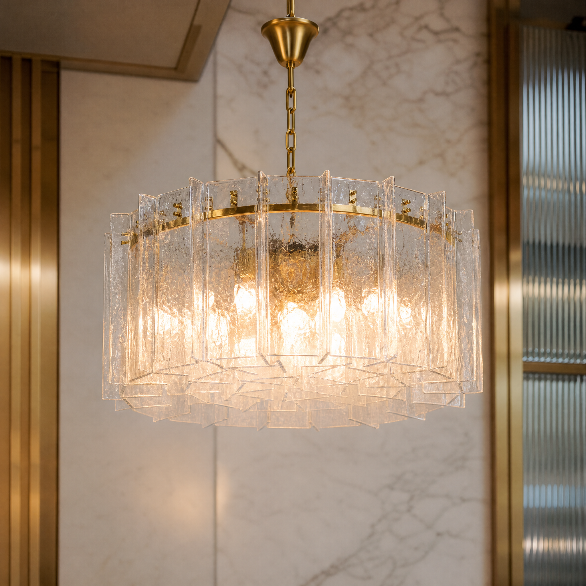 Macro shot of the VORELLI Berlinio chandelier showing detailed thick moulded Murano-style clear glass slabs bolted to a premium brass frame.
