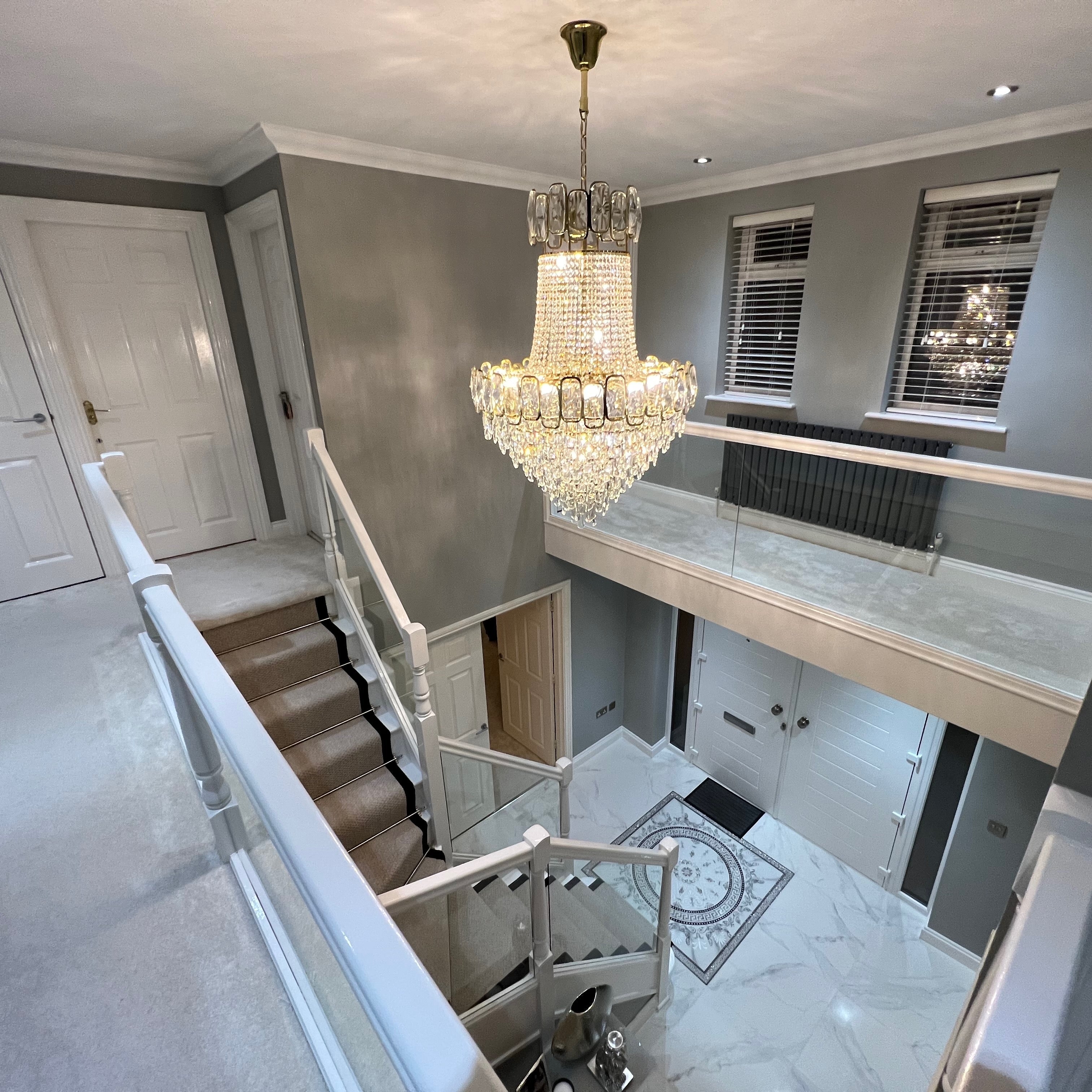 VORELLI Edison Grandeur staircase chandelier in a luxury double-height stairwell with cascading diamond-cut crystal tiers and warm ambient glow.