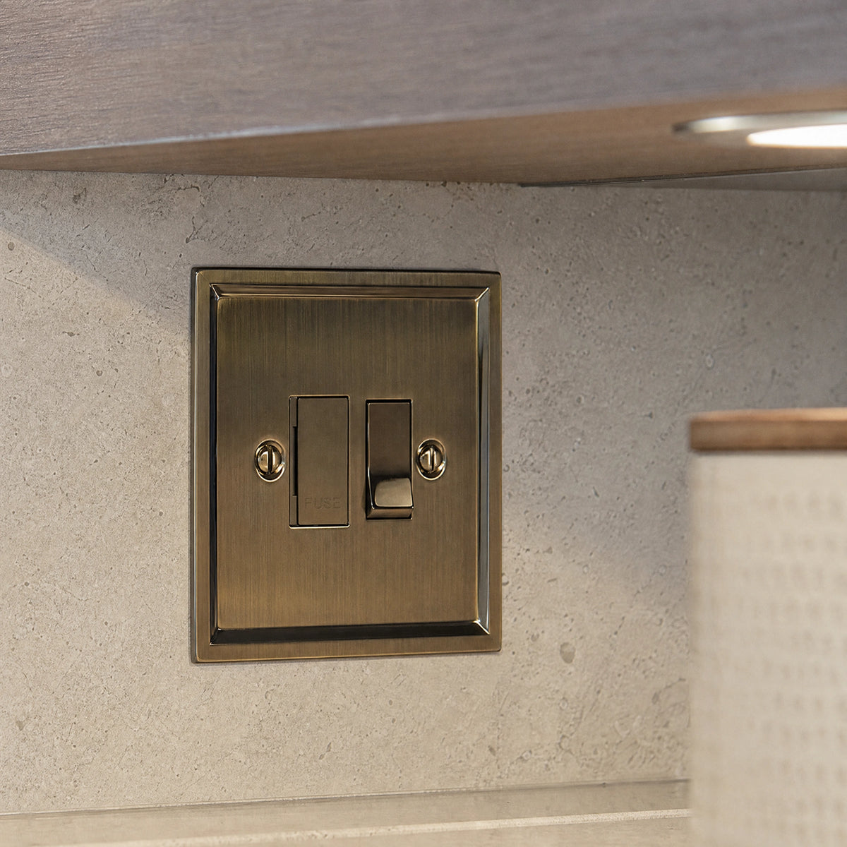 Close-up of a luxury antique brass fused spur installed within discreet below-cabinet utility or kitchen appliance zone in a high-end residence by VORELLI®.