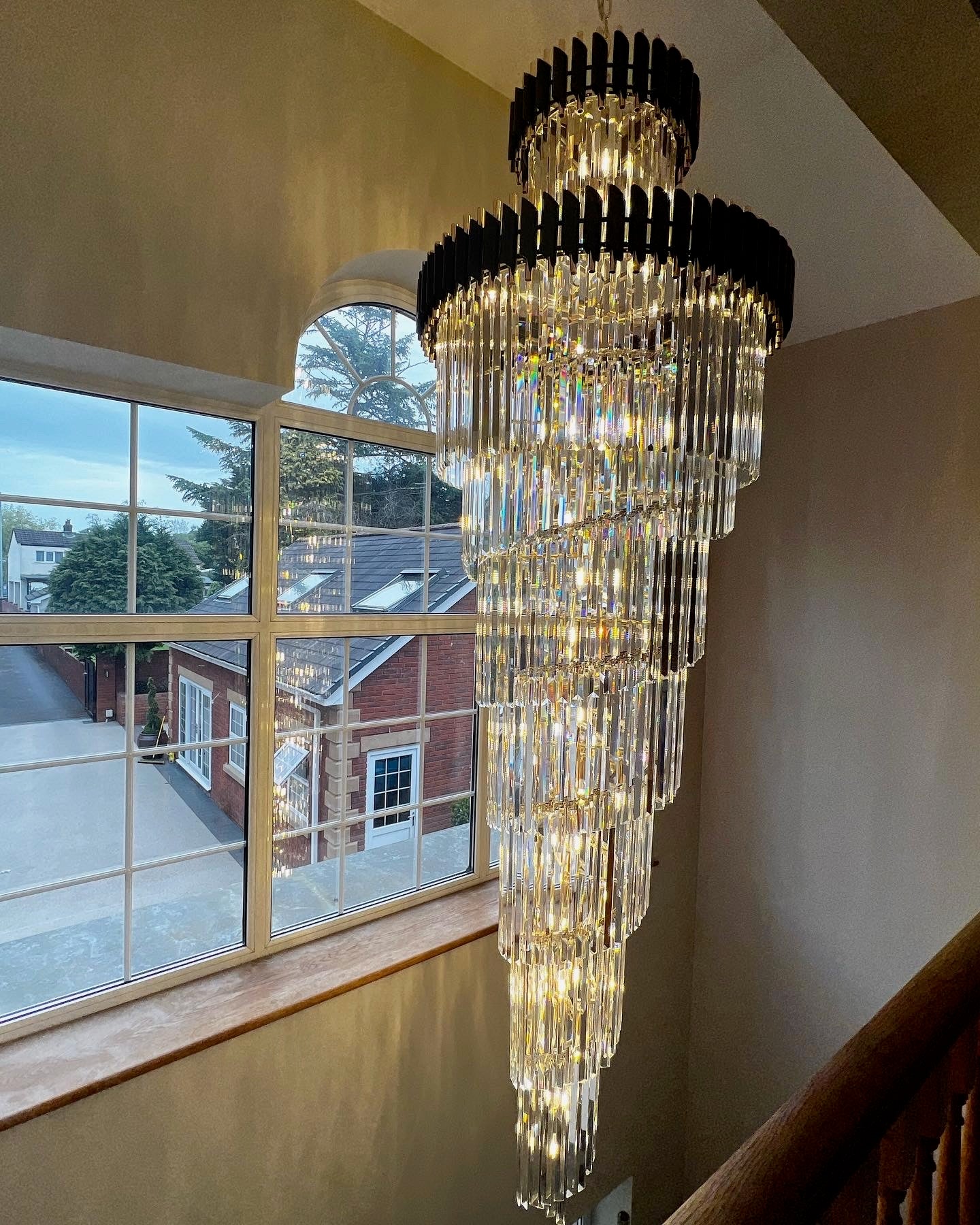 Long crystal staircase chandelier by VORELLI® illuminating a multi-storey grand stairwell