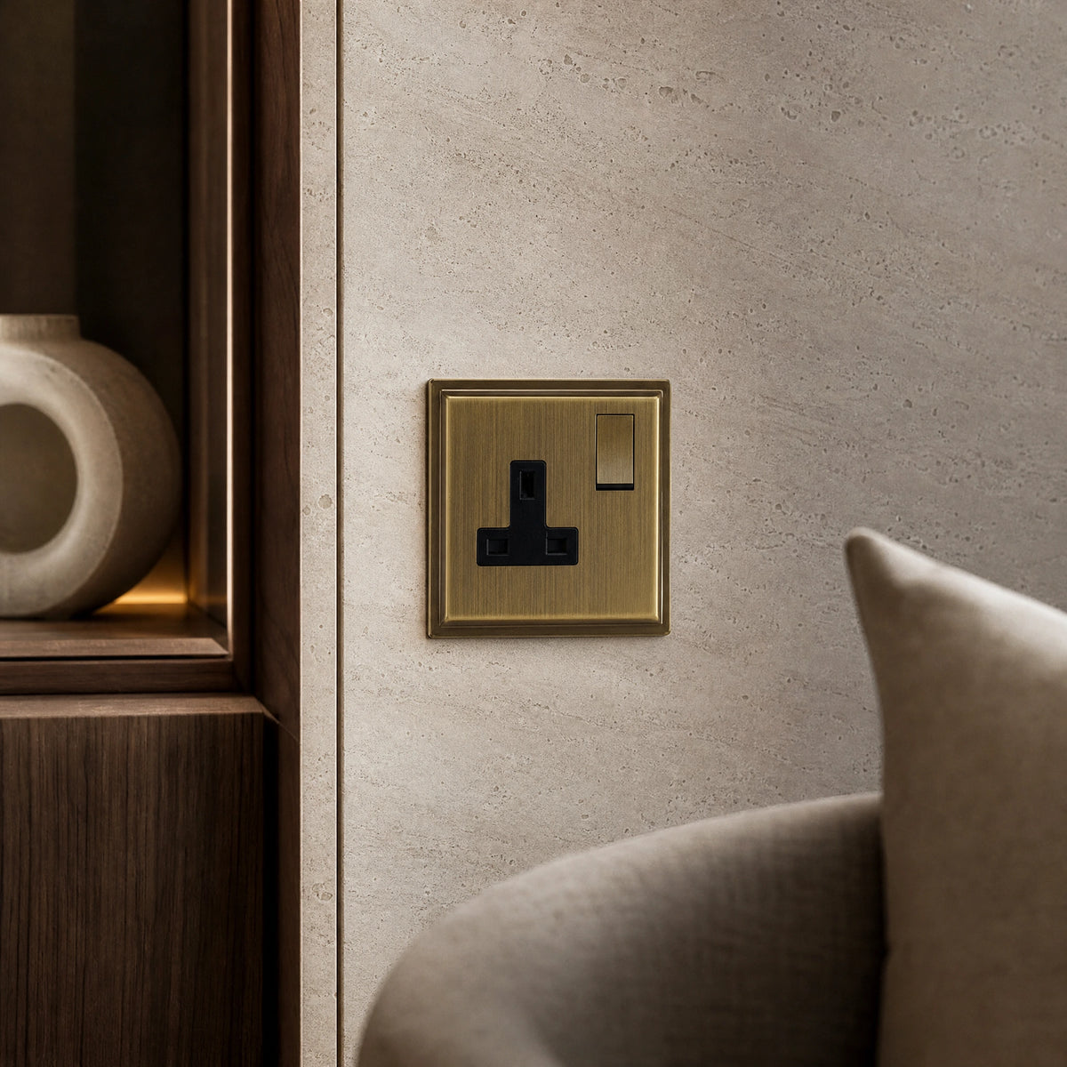 Close-up of a luxury antique brass single socket installed within bespoke bedside joinery or stone wall beside a luxury seating area by VORELLI®.