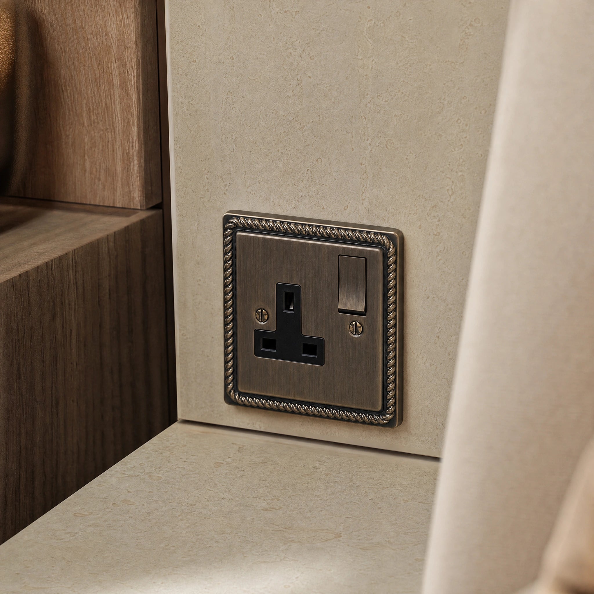Close-up of a luxury antique brass single socket installed within bespoke bedside joinery or stone wall beside a luxury seating area by VORELLI®.