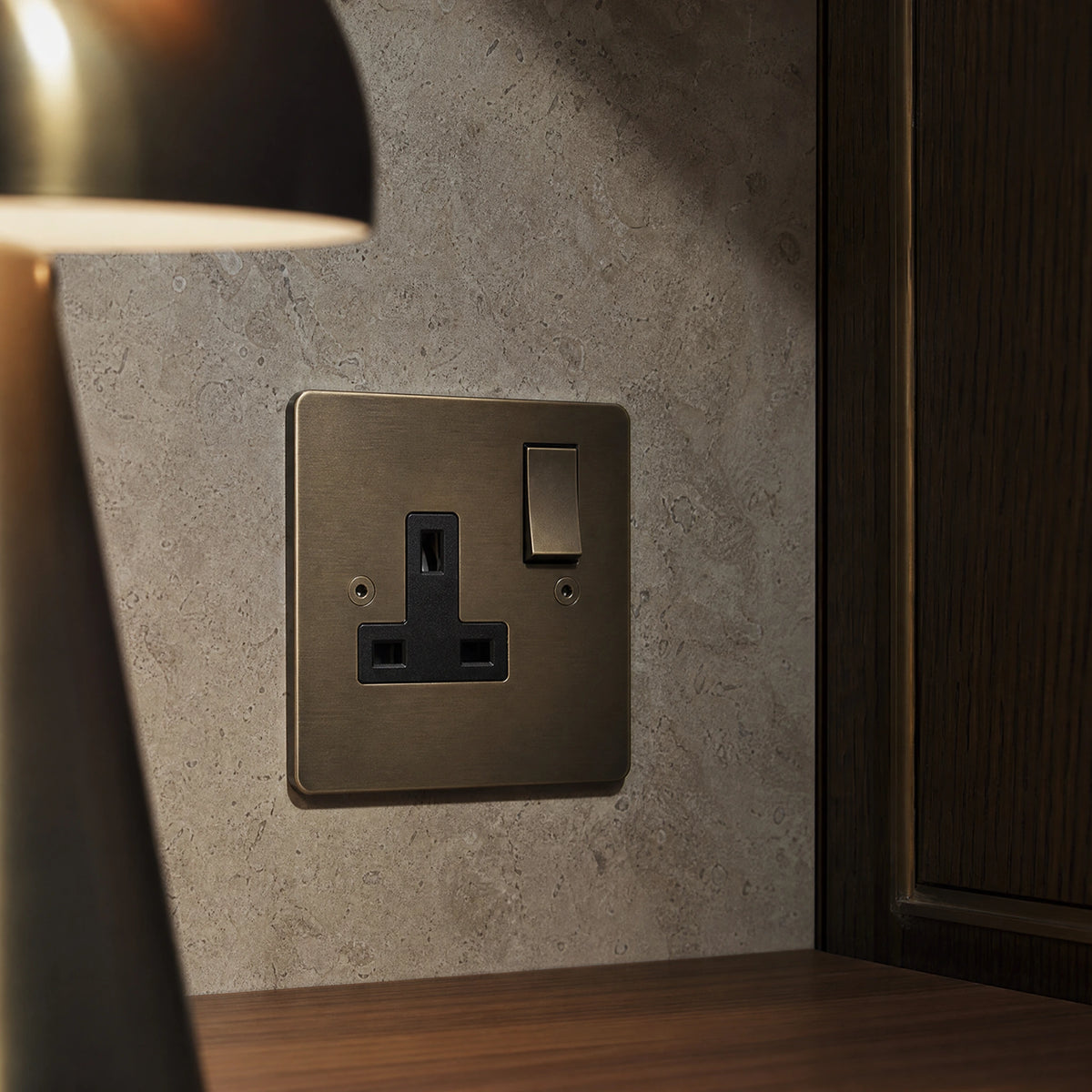 Close-up of a luxury antique brass single socket installed within bespoke bedside joinery or stone wall beside a luxury seating area by VORELLI®.