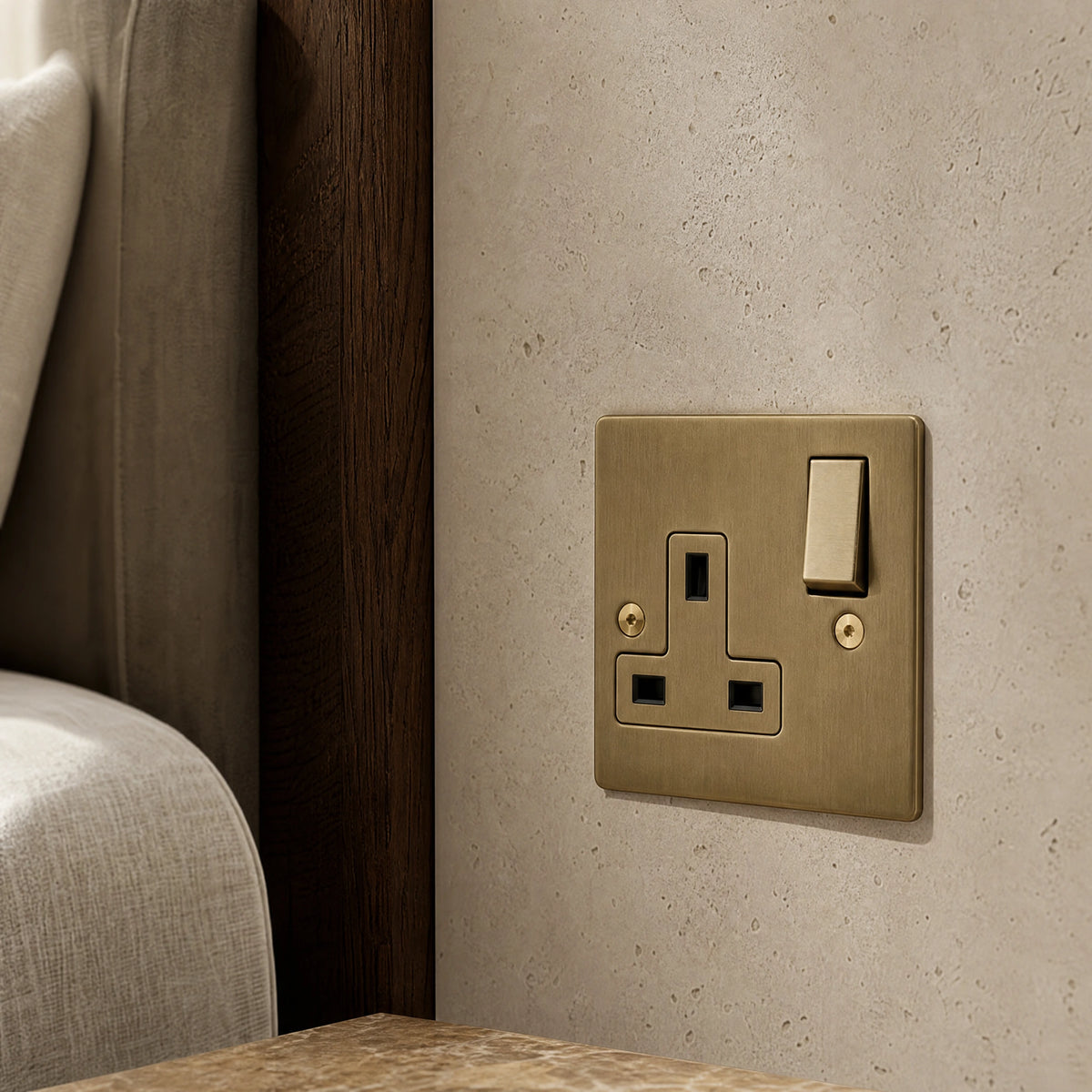 Close-up of a luxury antique brass single socket installed within bespoke bedside joinery or stone wall beside a luxury seating area by VORELLI®.