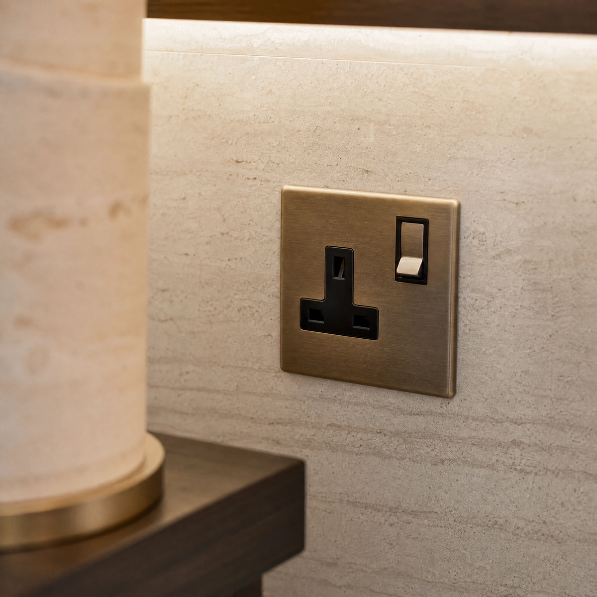 Close-up of a luxury antique brass single socket installed within bespoke bedside joinery or stone wall beside a luxury seating area by VORELLI®.