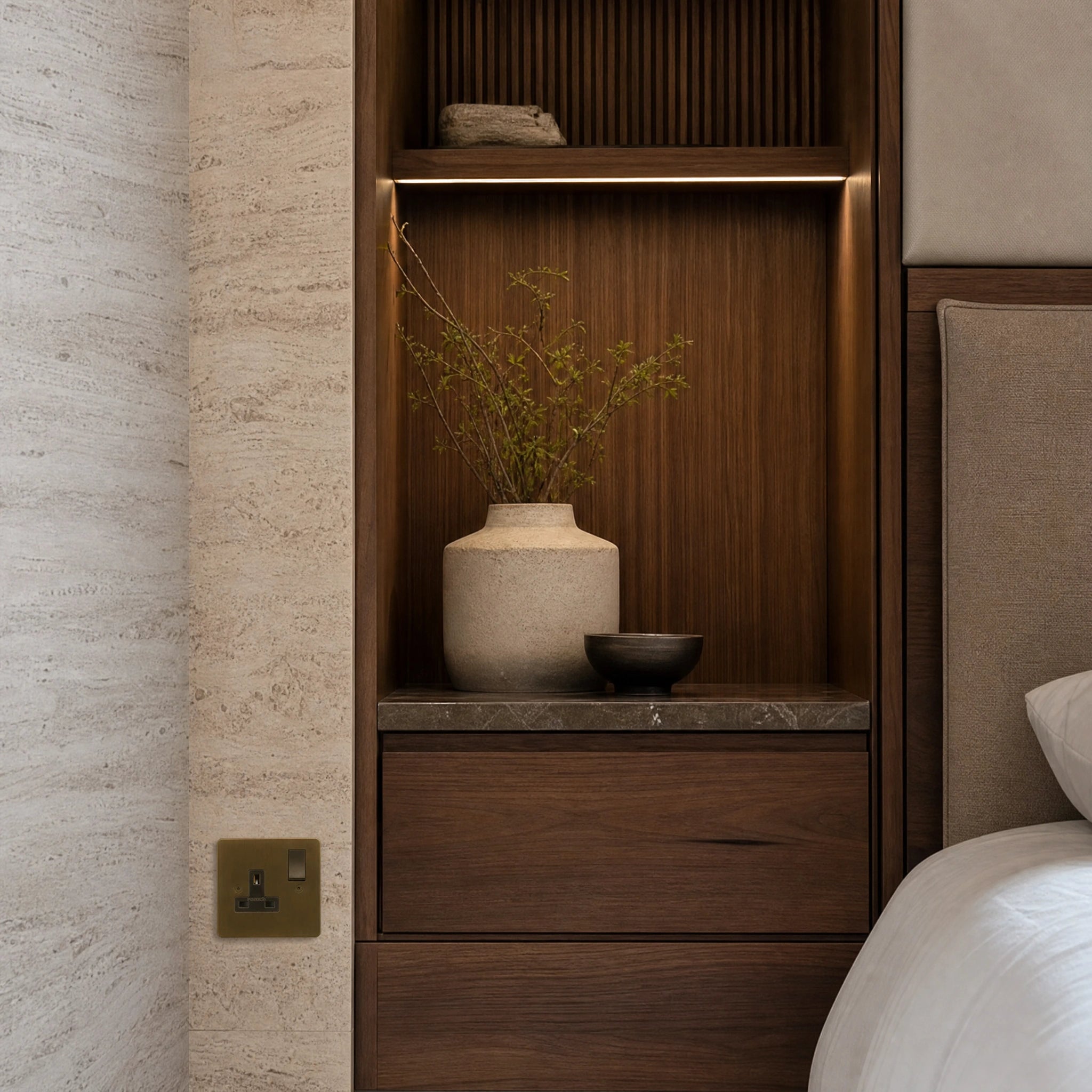 Luxury antique brass single socket installed within bespoke bedside joinery or stone wall beside a luxury seating area in a UHNW interior by VORELLI®.