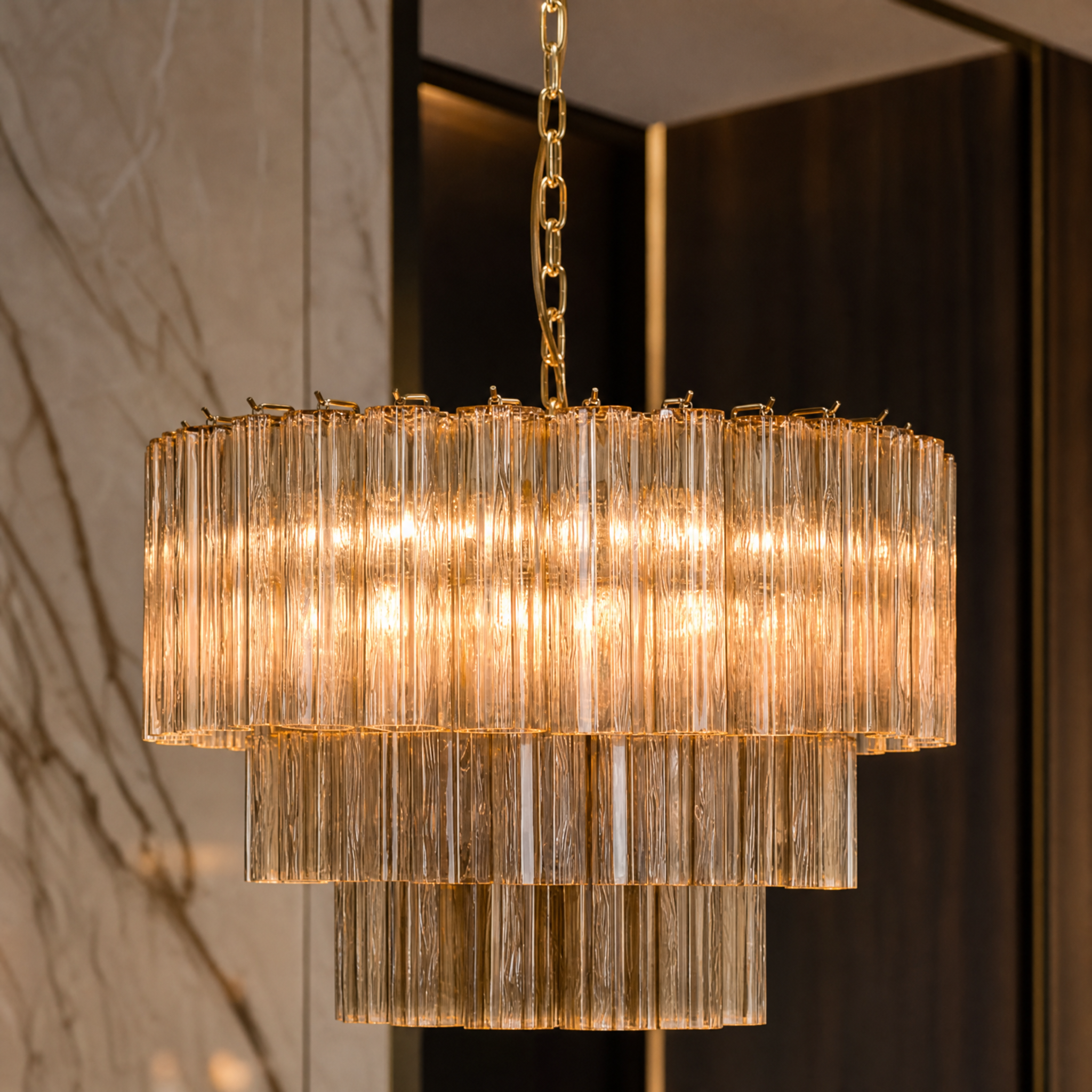 Detailed macro shot of VORELLI Trevisano chandelier showcasing amber Murano fluted glass tubes suspended on a satin brass frame.
