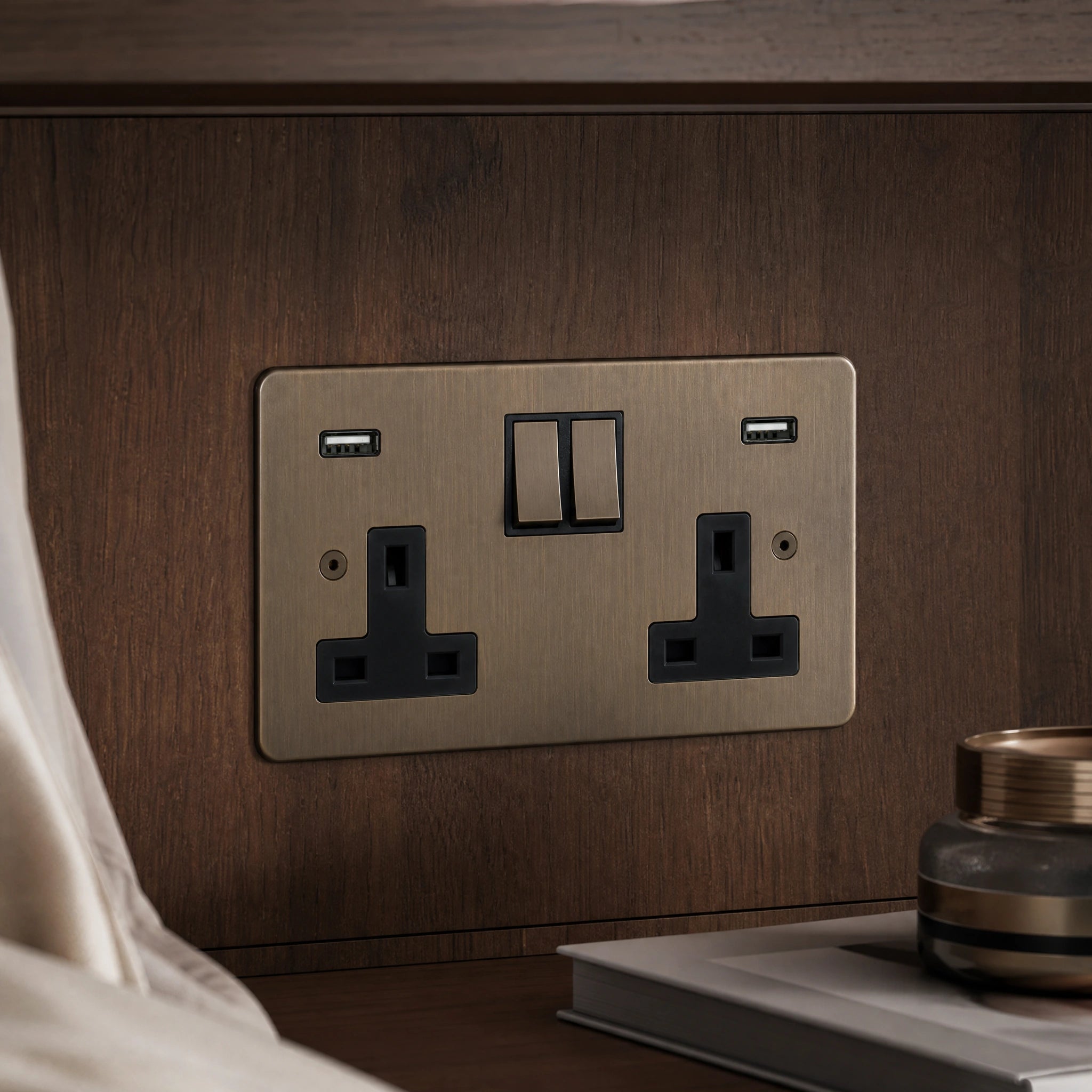 Close-up of a luxury antique brass double socket with USB charging installed within bespoke walnut bedside joinery by VORELLI®.