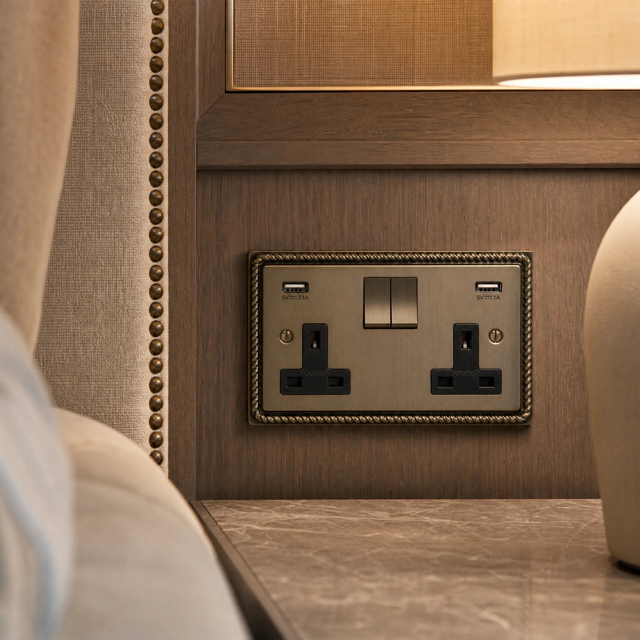 Close-up of a luxury antique brass usb socket installed within bespoke bedside joinery in a luxury bedroom suite by VORELLI®.