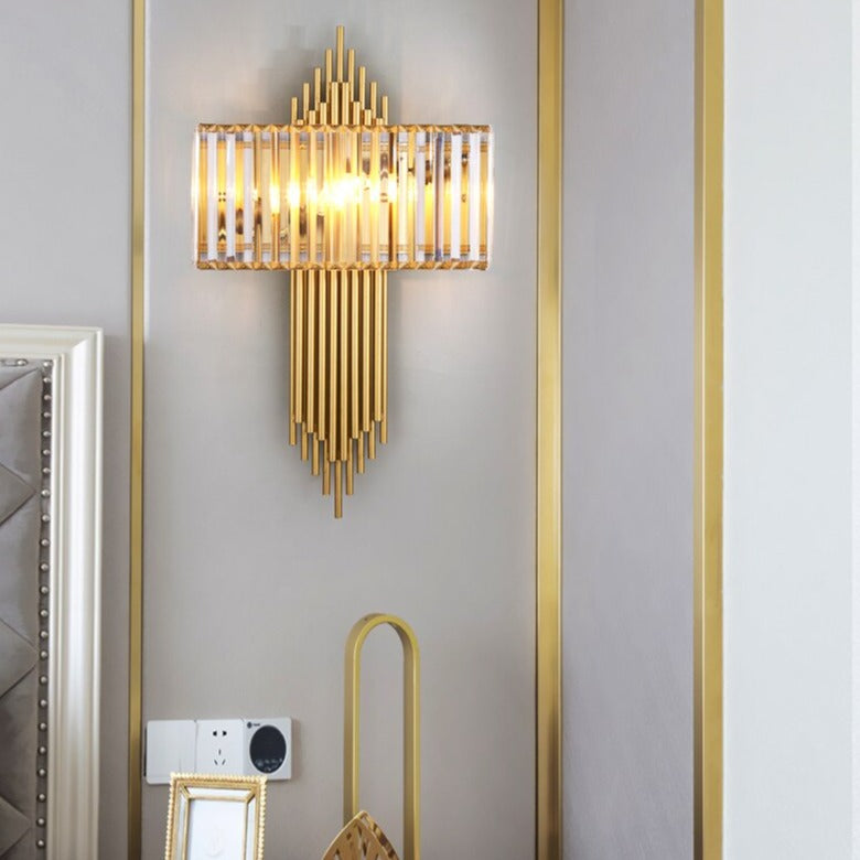 Gold Alora wall light with vertical crystal bars, mounted on a decorative panelled wall.
