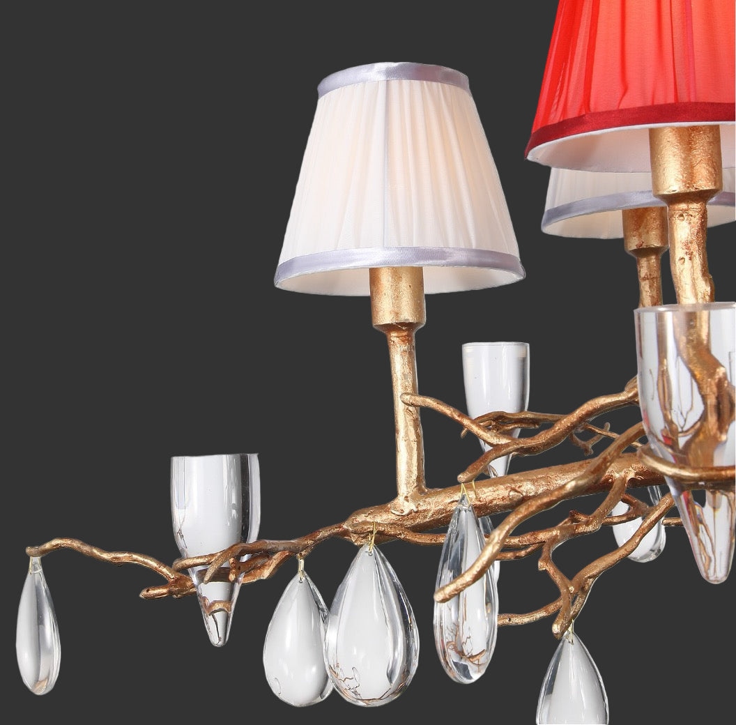 Gold chandelier detail with white and red lampshades and droplet crystals.