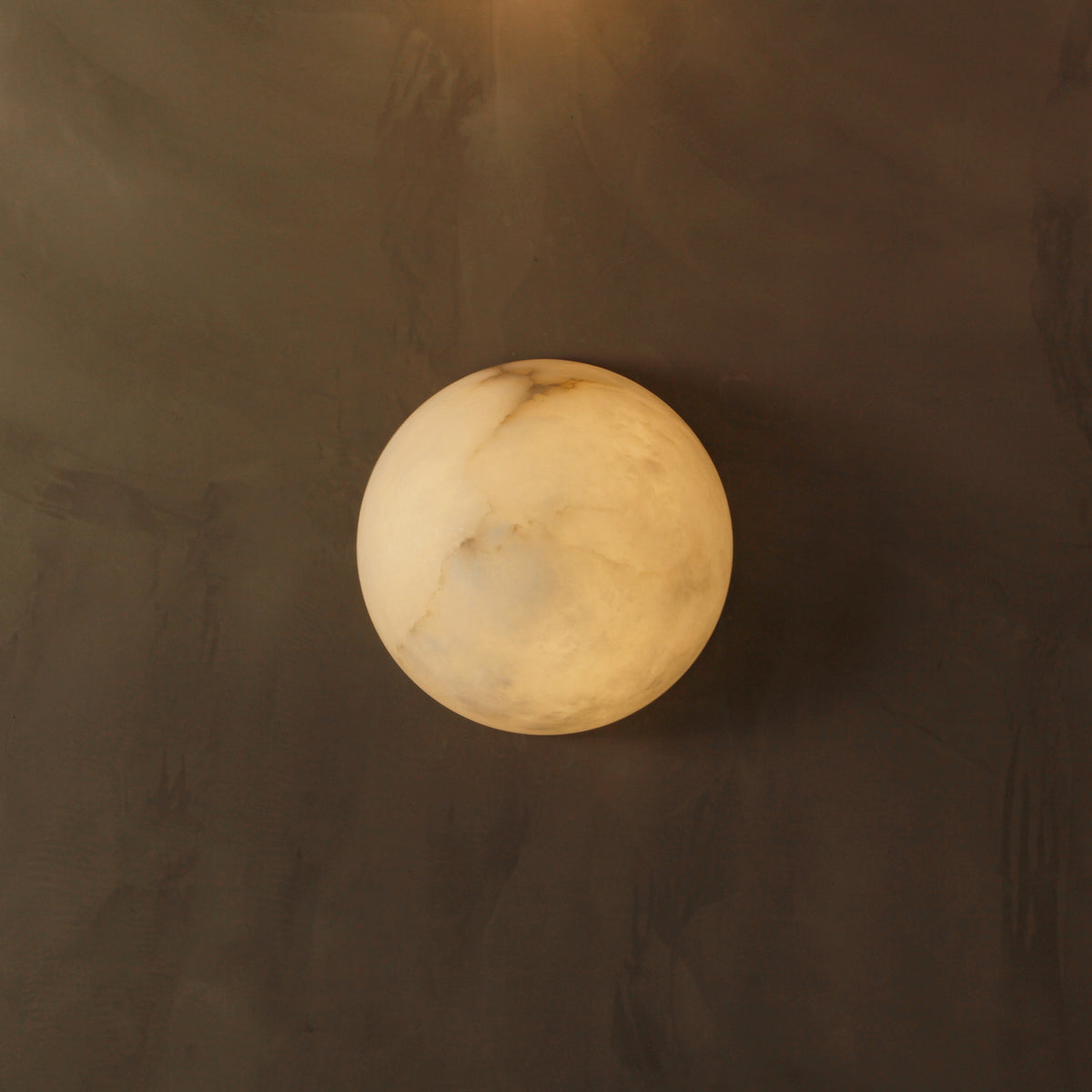Close-up of the Arona light’s smooth oval marble design against a textured wall.