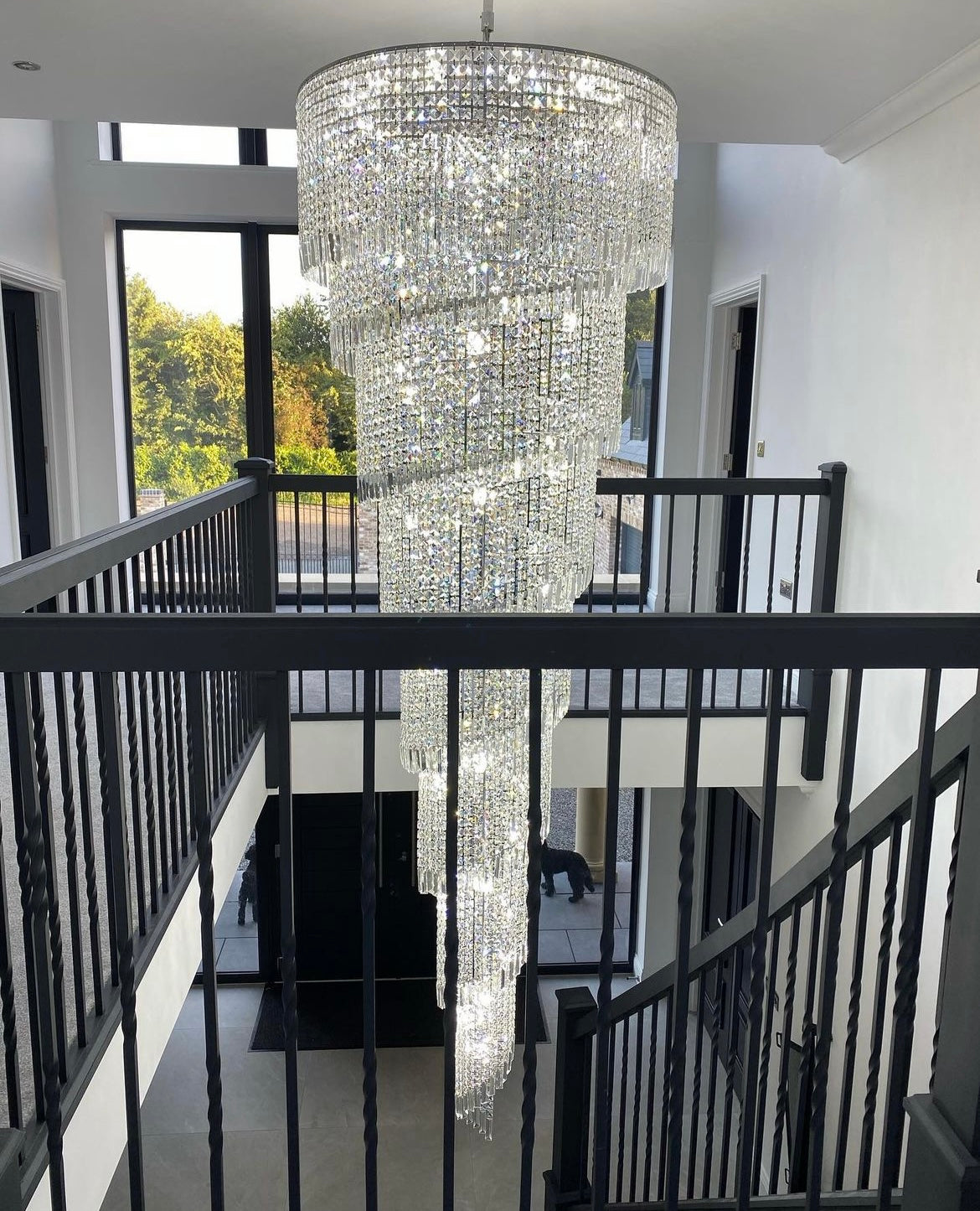 Elegant crystal formation of the Basilgio chandelier suspended in a contemporary stairwell.