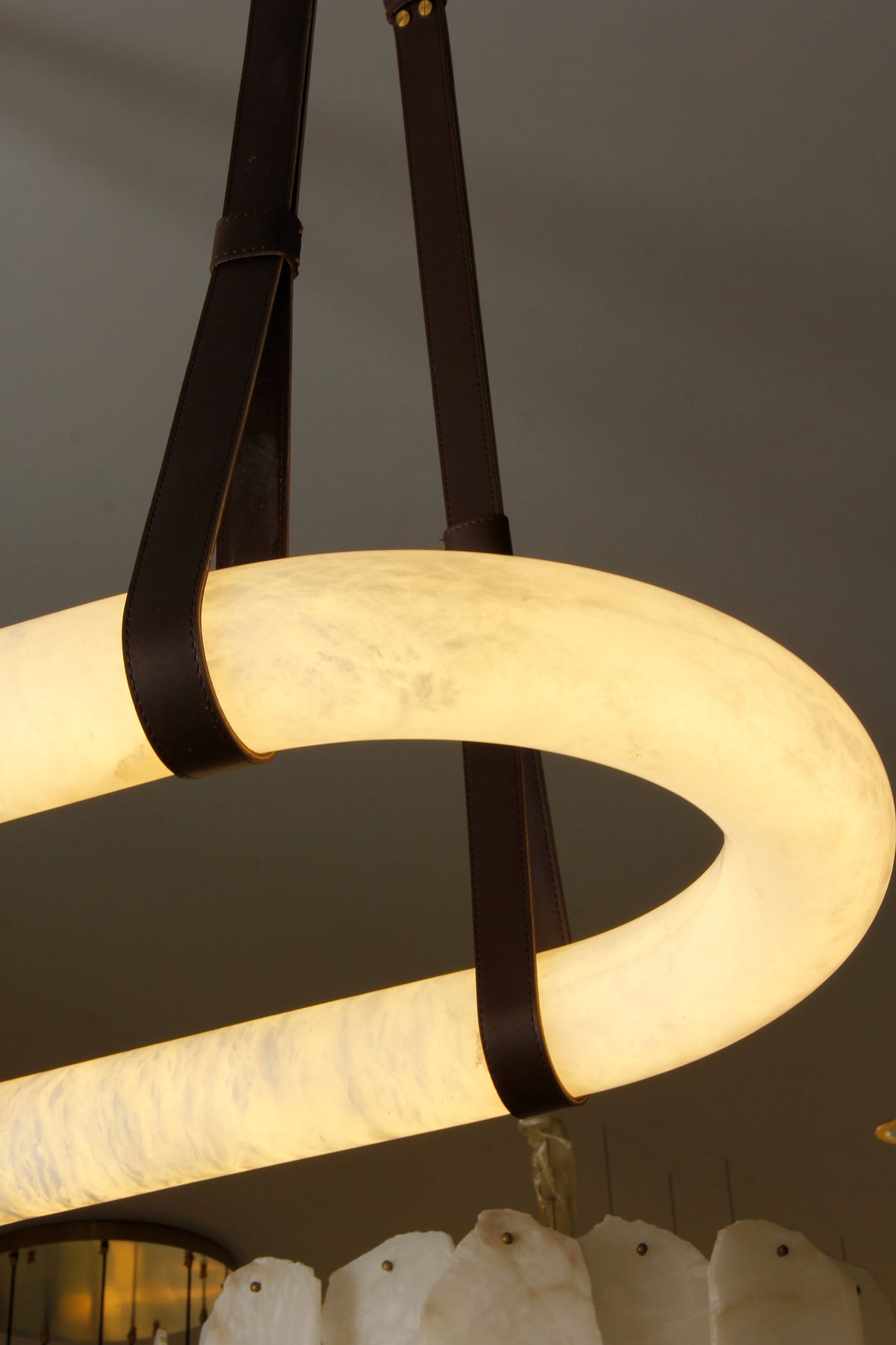 Side view of the Botticino Marble Rectangular Chandelier showing the glowing marble surface and leather straps.