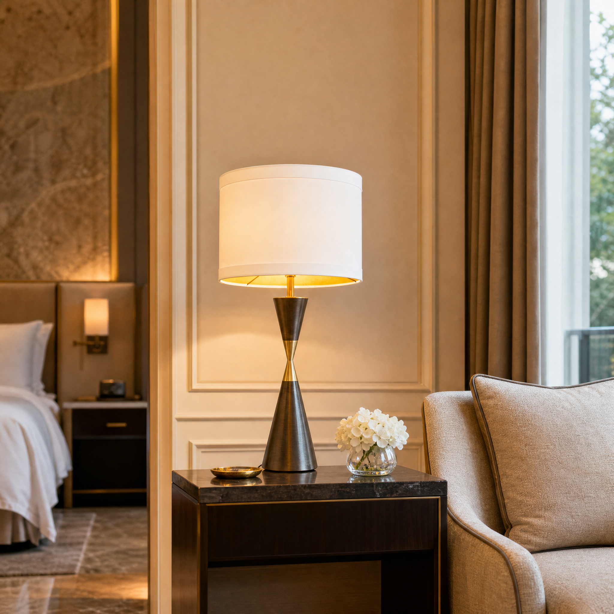 The elegant Dalmora table lamp by VORELLI casting a warm glow on a concierge desk in a high-end boutique hotel lobby.