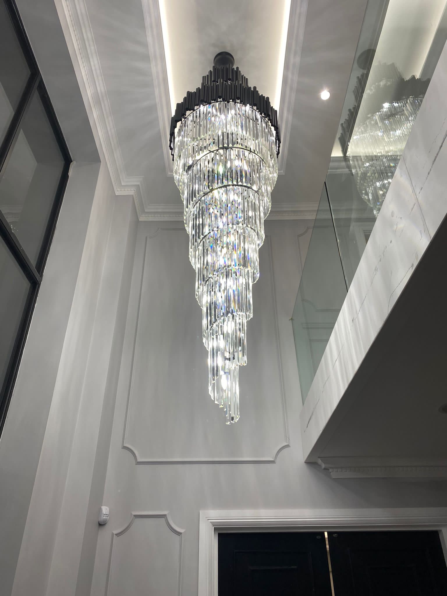 Long tiered crystal staircase chandelier illuminating a double height luxury interior