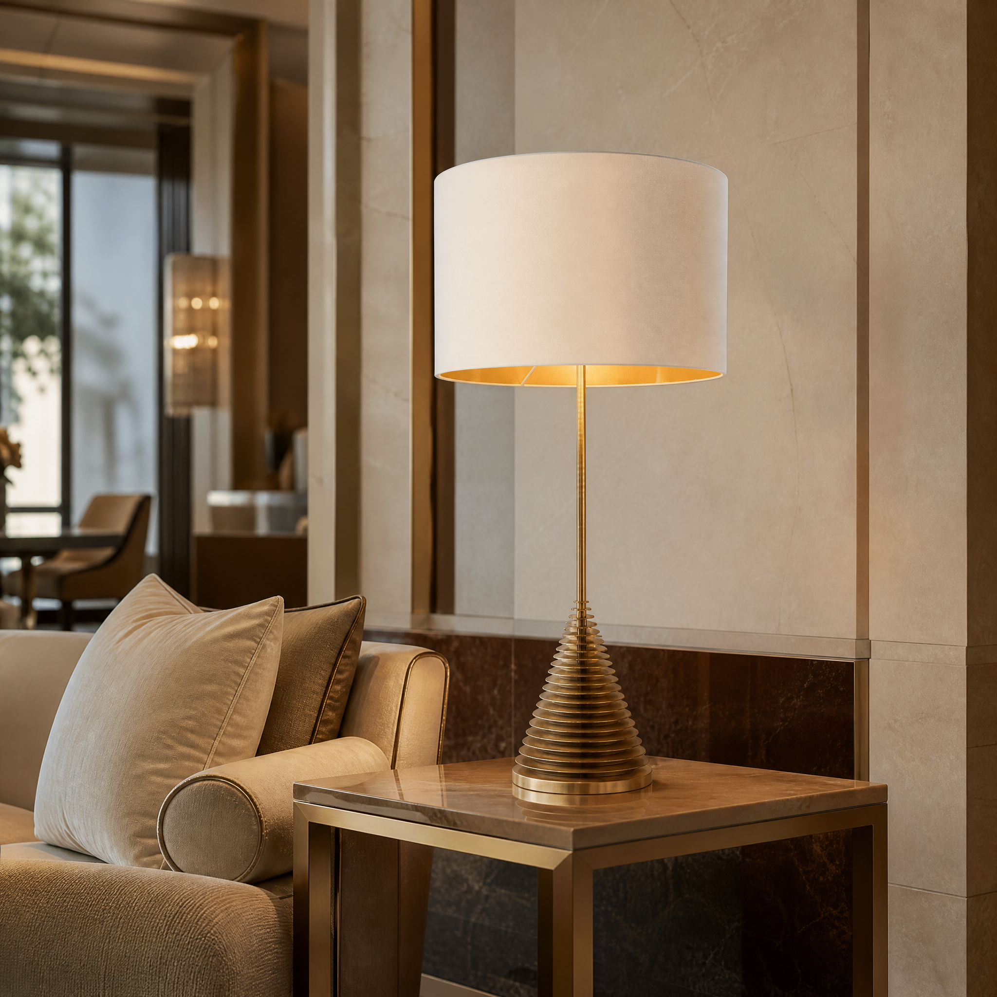 The elegant vertical silhouette of the Orviano tall brass table lamp casting a warm glow in a sophisticated boutique hotel lounge.