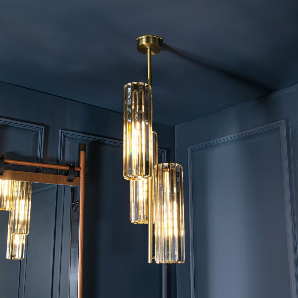 Reagan triple crystal pendant light cluster suspended in refined interior featuring three vertical faceted crystal cylinders