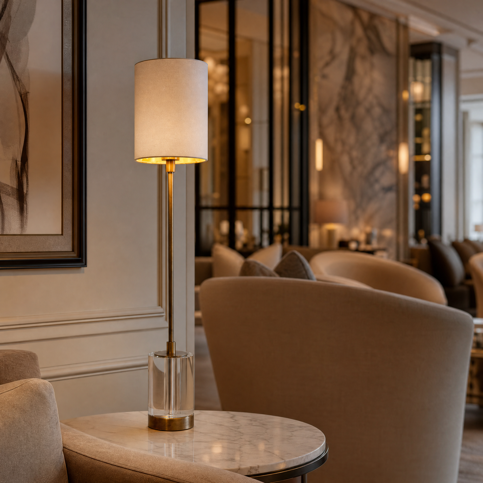 An elegant VORELLI Renvaro brass table lamp with a clear crystal base adding understated luxury to a sophisticated hotel hospitality lounge.