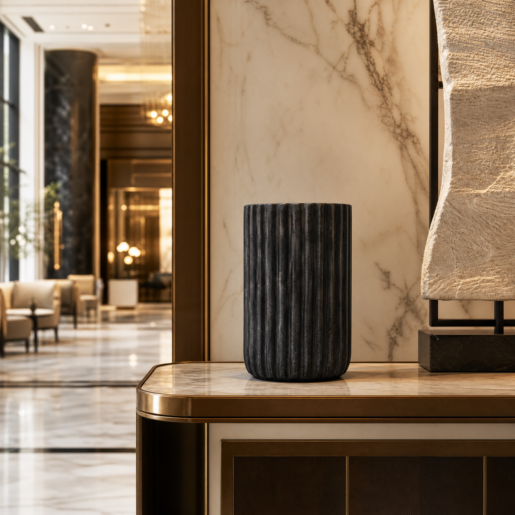 A sophisticated hospitality display featuring the Solaro black marble ribbed decorative vase on a reception desk in a contemporary hotel lobby.