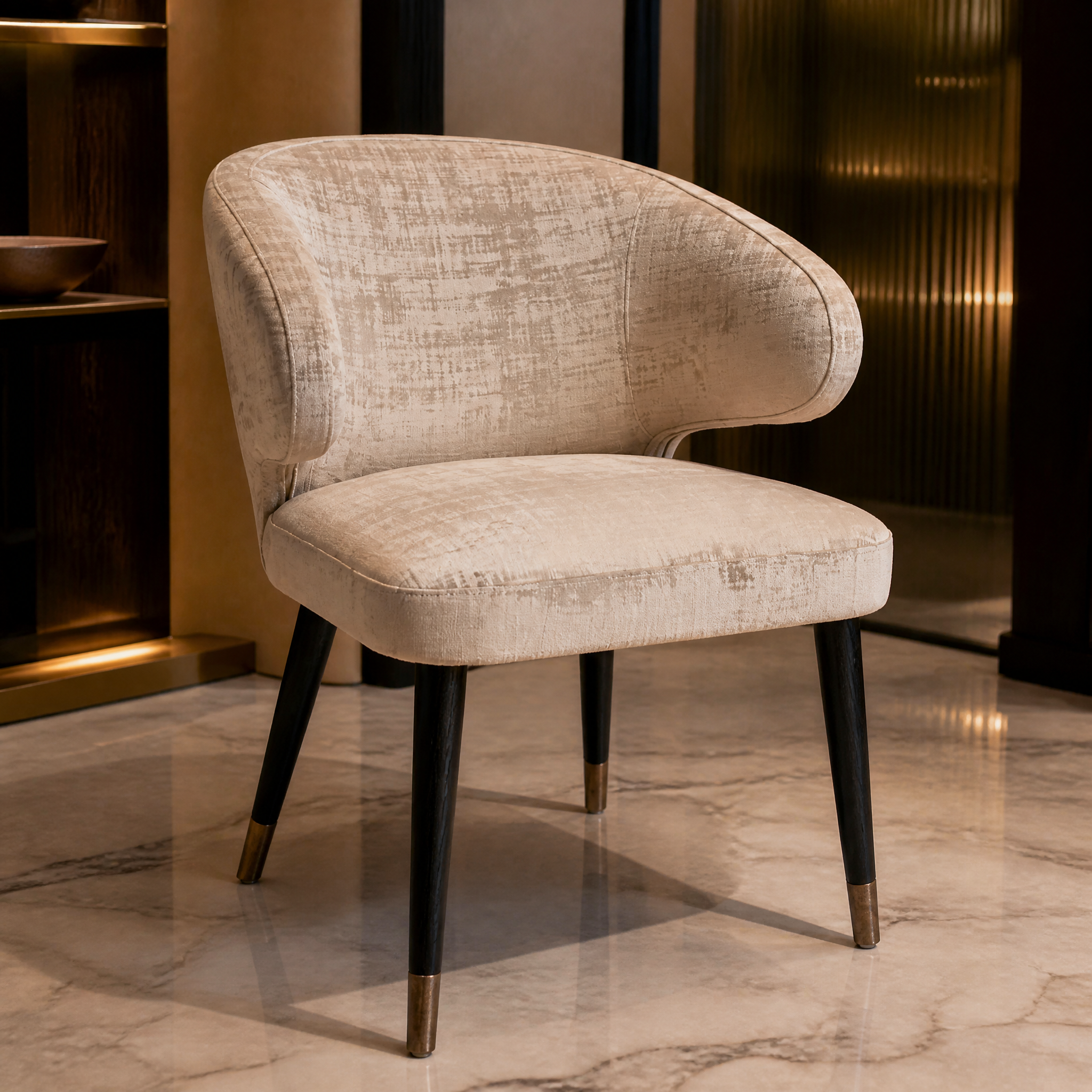 Detailed closeup of the VORELLI Spencer chair showcasing the sumptuous luxe mushroom upholstery texture and refined warm brass trim.