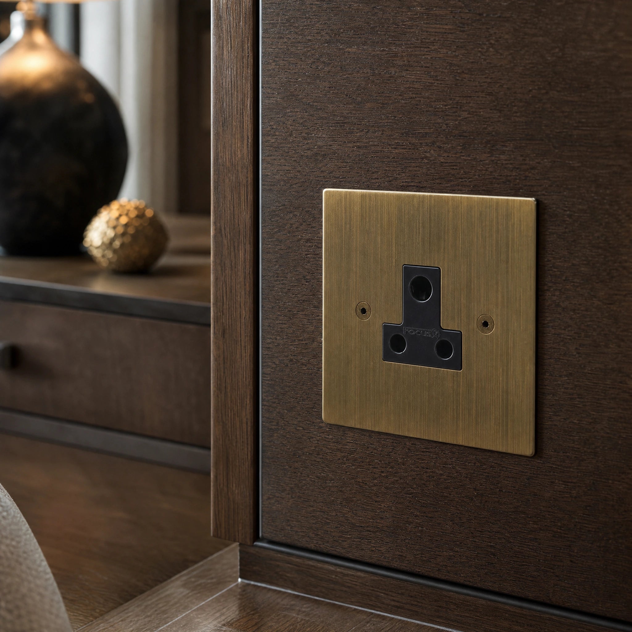 Close-up of a luxury antique bronze 5a socket installed within bespoke bedside joinery or low-level wall beside a luxury seating area by VORELLI®.