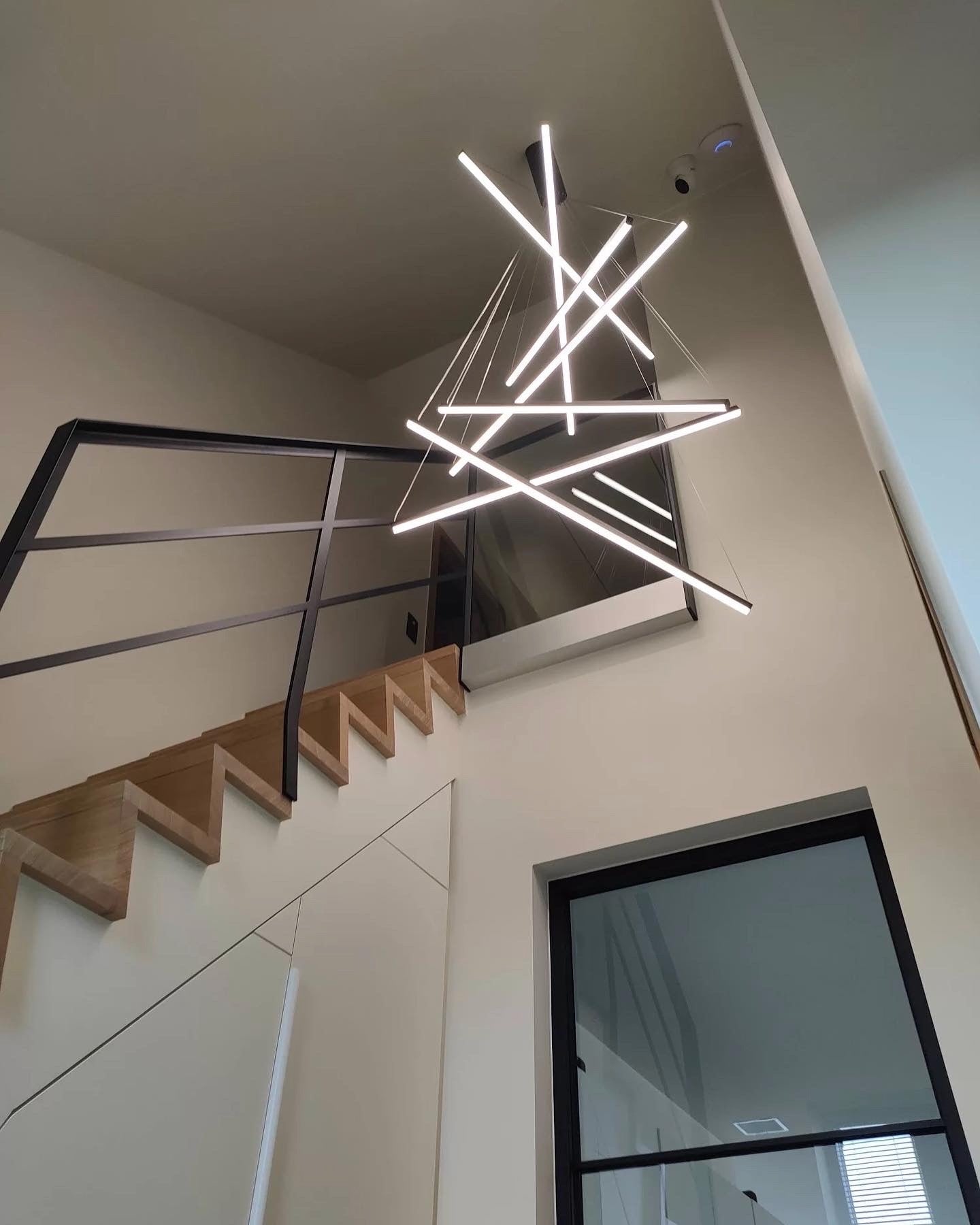 Linear LED pendant chandelier illuminating a tall double height residential staircase