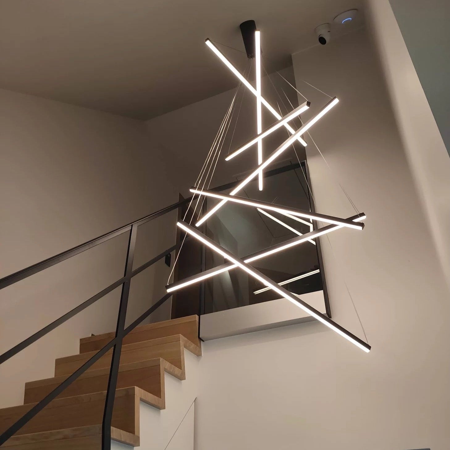 Luxury modern linear LED pendant staircase chandelier installed in a contemporary stairwell interior by VORELLI®